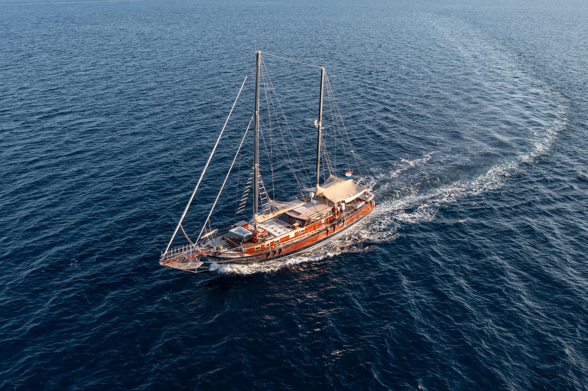 aerial view of wooden gulet with two masts sailing through deep blue waters