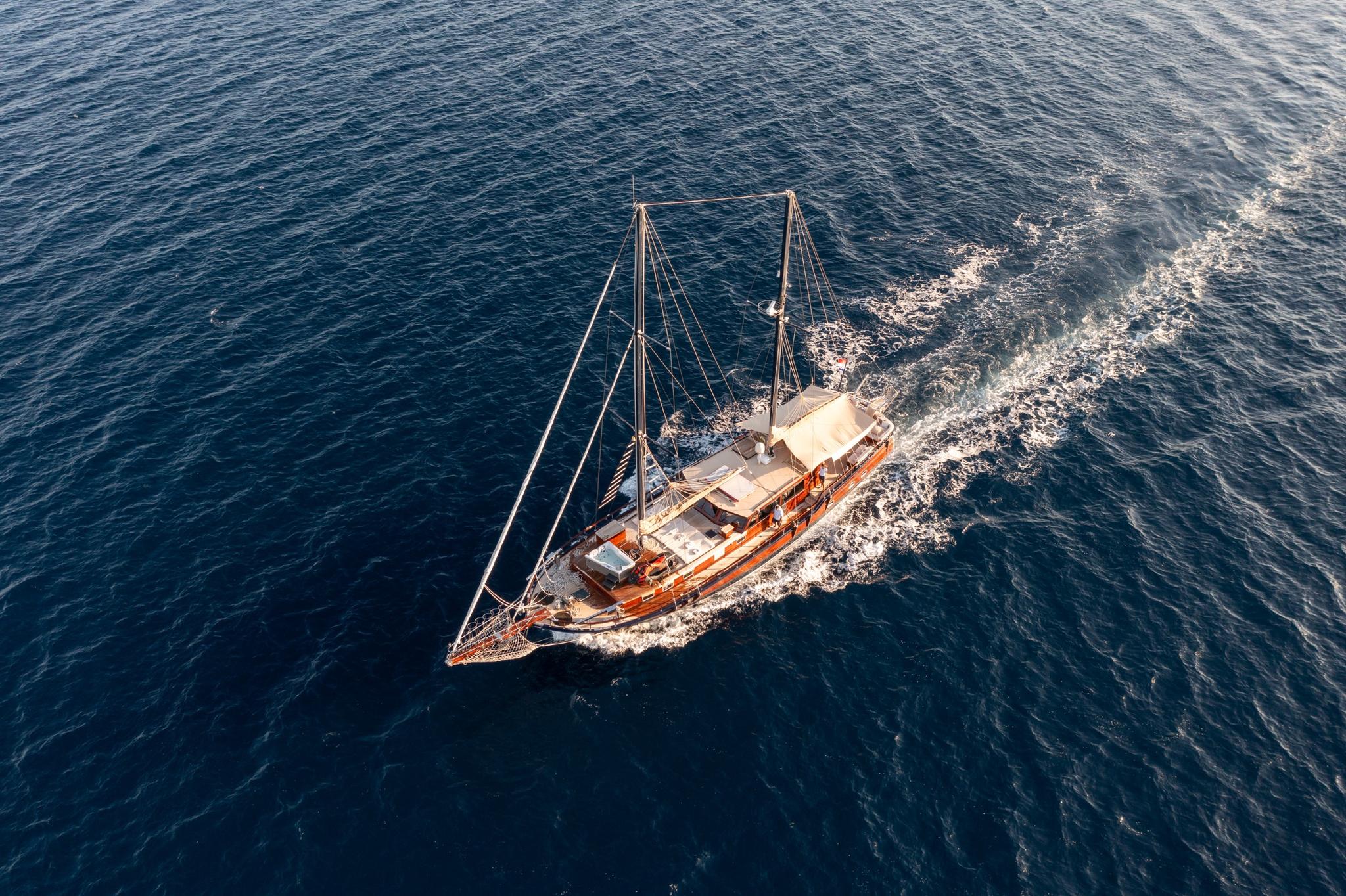 aerial view of traditional wooden gulet yacht with two masts underway creating white wake