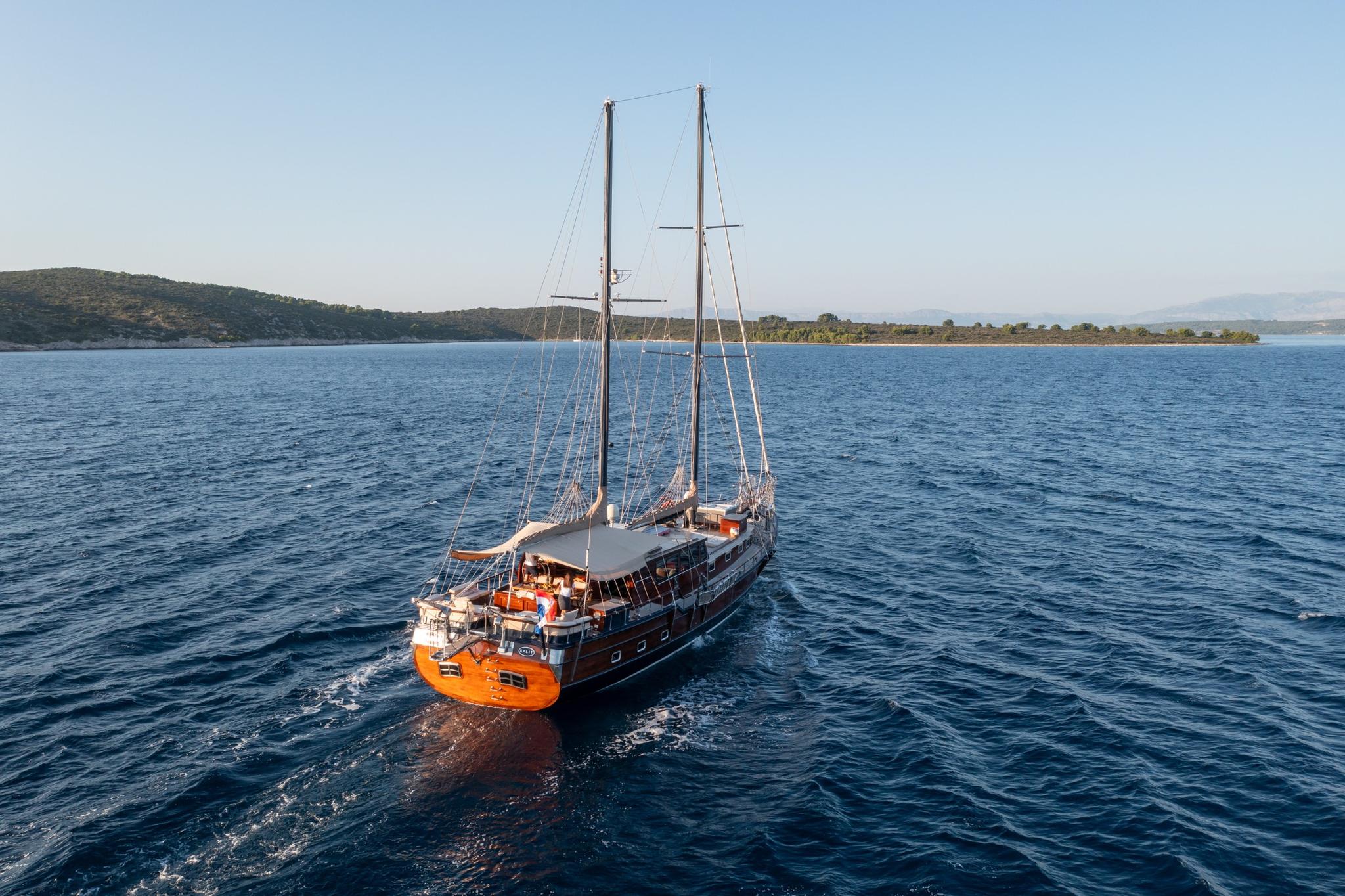 wooden gulet yacht with two masts anchored in blue Mediterranean bay with coastline