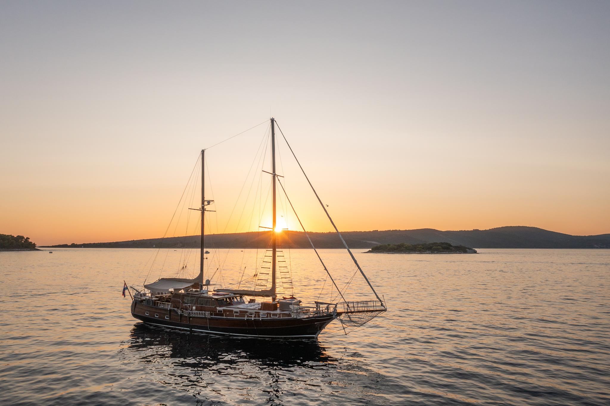 Traditional wooden gulet with two masts and rigging anchored at golden sunset