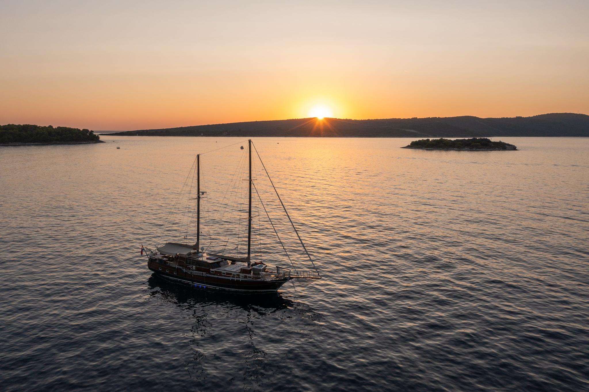 Traditional gulet yacht with two masts anchored in calm waters during golden sunset
