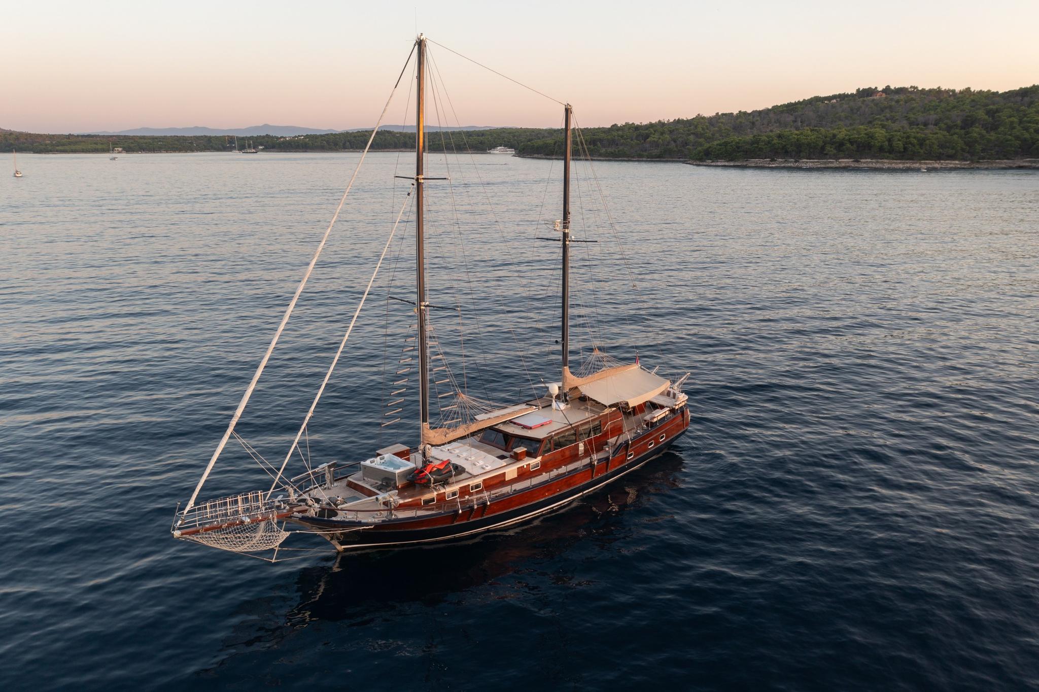aerial view of traditional wooden gulet with two masts anchored in sheltered bay at sunset
