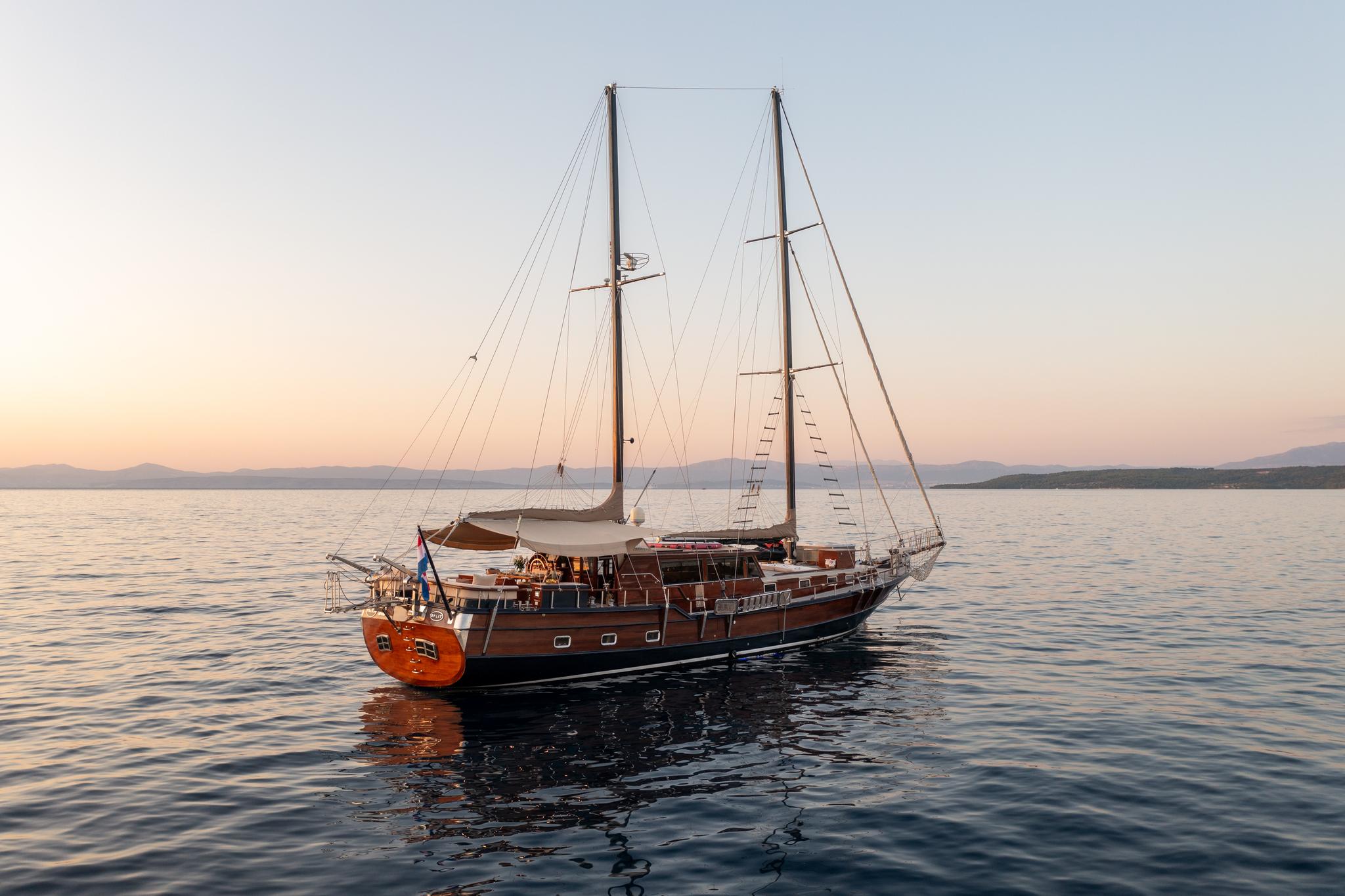 Traditional wooden gulet with two masts anchored in calm waters at sunset