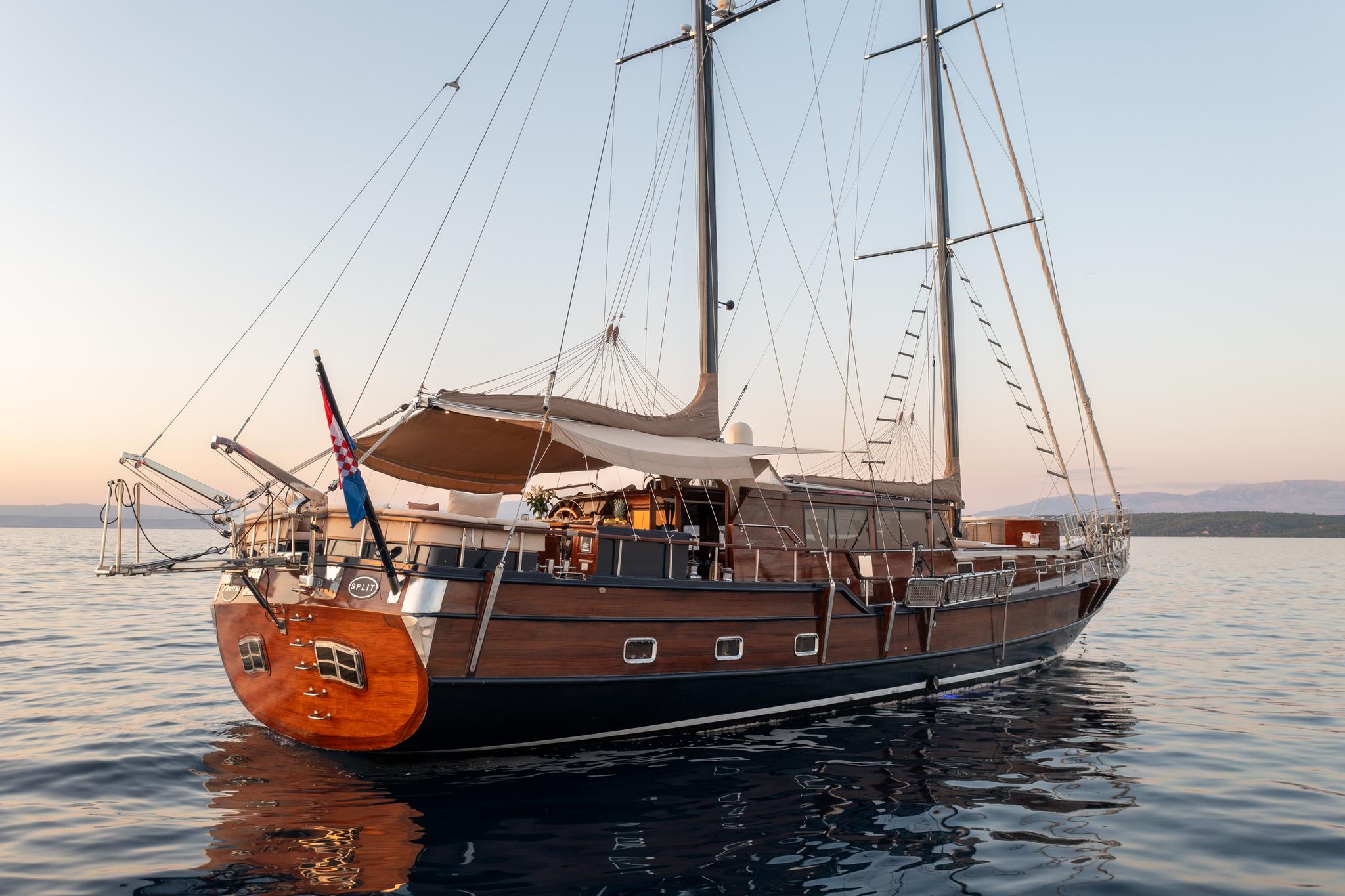 Traditional wooden gulet with two masts and rigging anchored in calm waters at sunset
