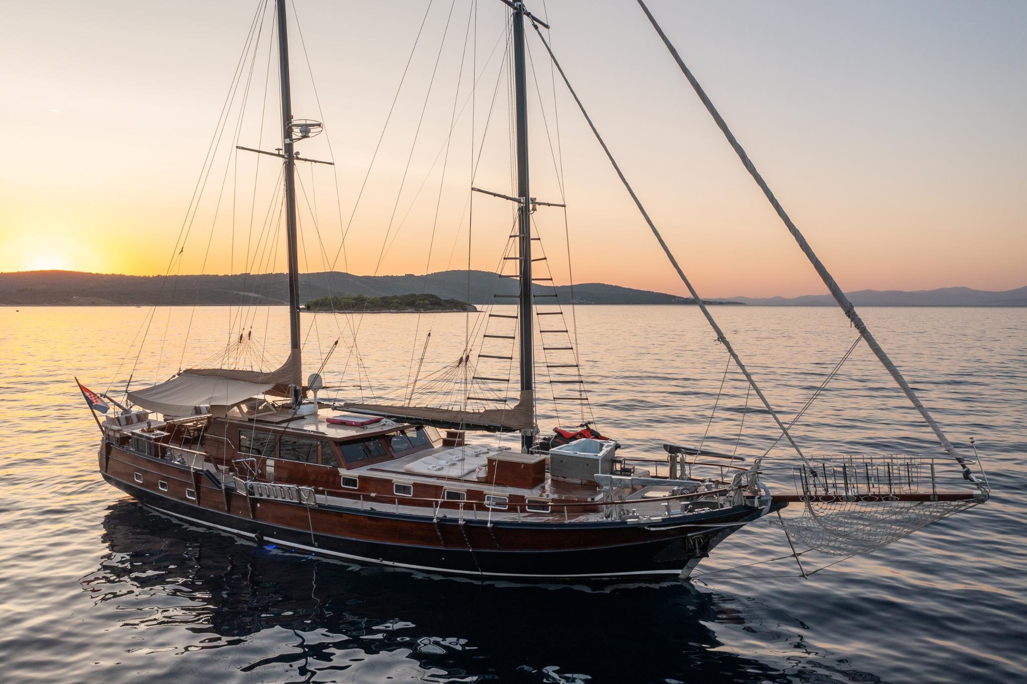 Traditional wooden gulet with two masts anchored at sunset with hills in background