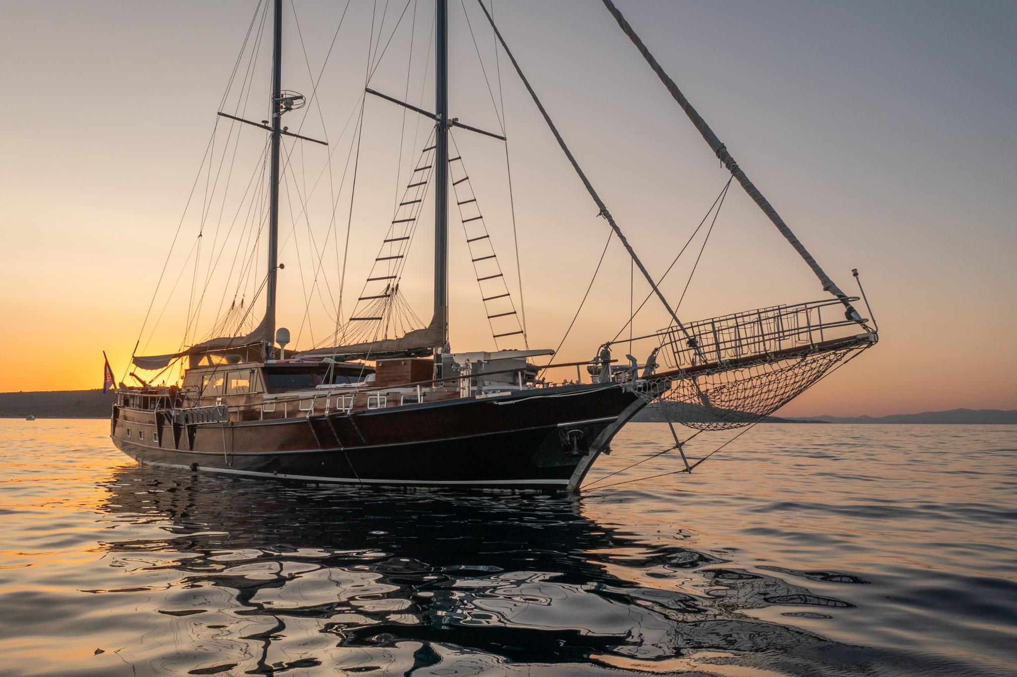 Traditional wooden gulet with two masts and rigging anchored at golden sunset