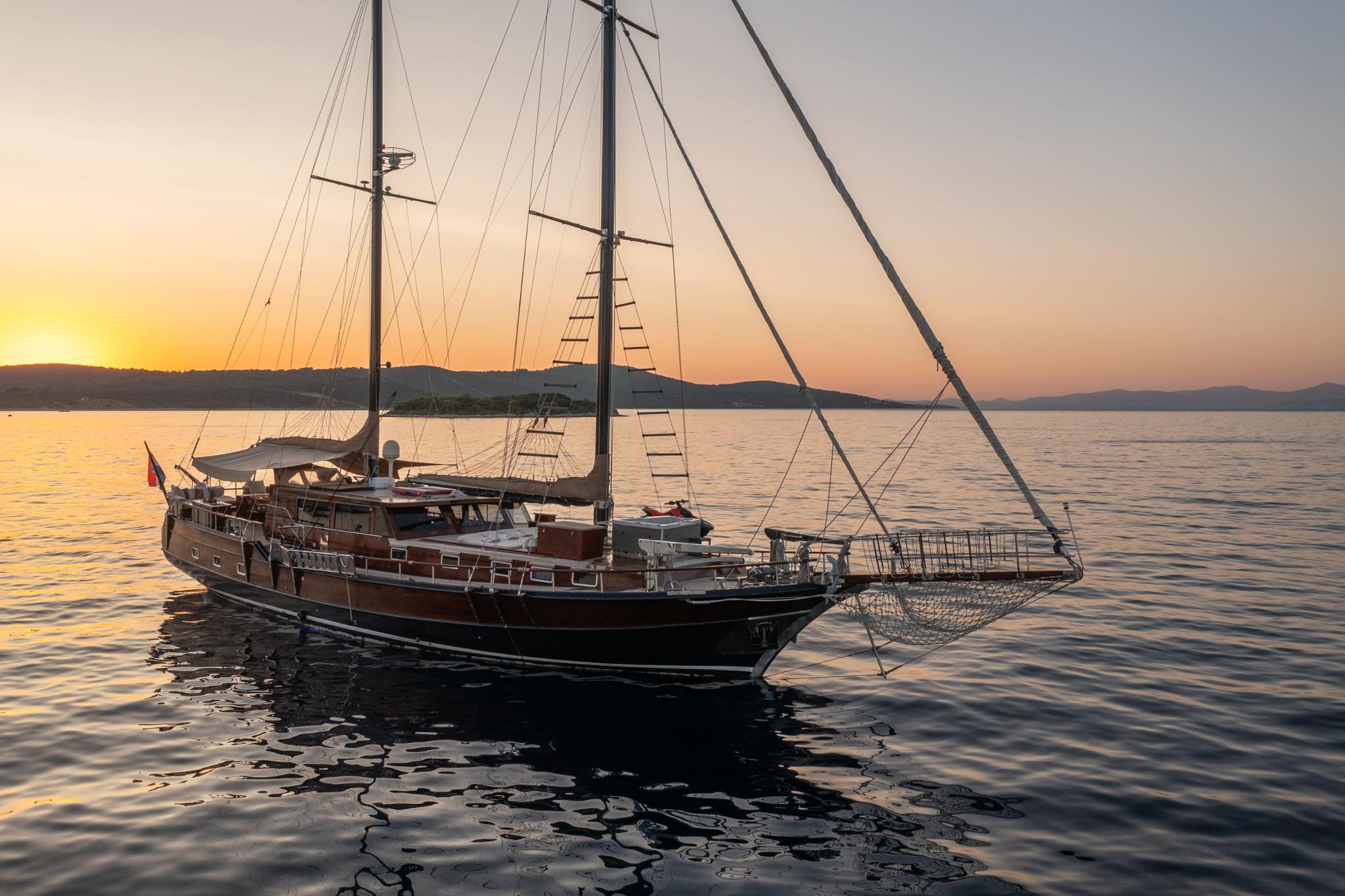 Traditional wooden gulet yacht anchored in calm waters during golden sunset with two masts