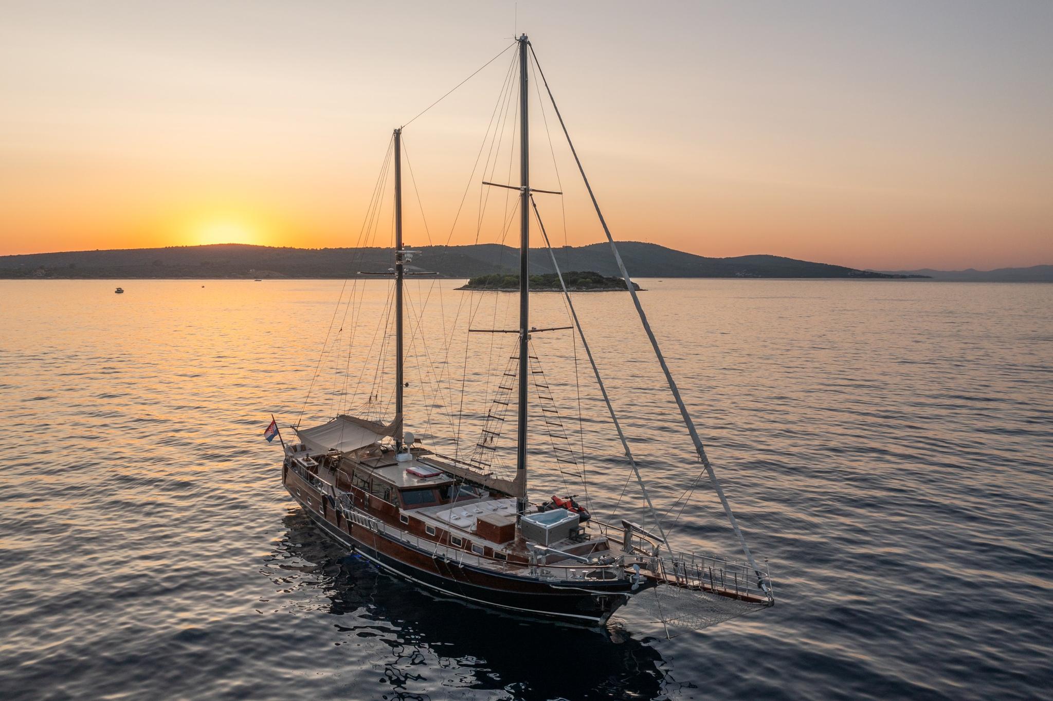 Traditional wooden gulet with two masts anchored in calm waters at sunset
