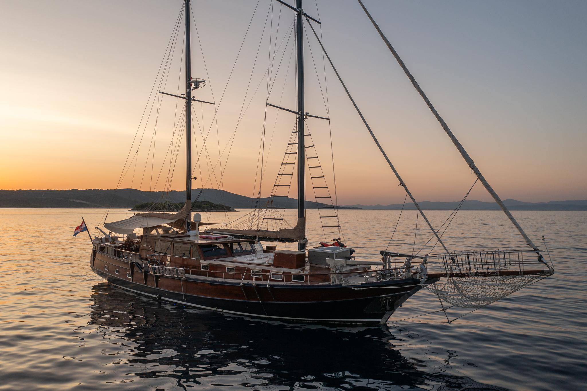 Traditional wooden gulet yacht with two masts anchored in calm waters at golden sunset