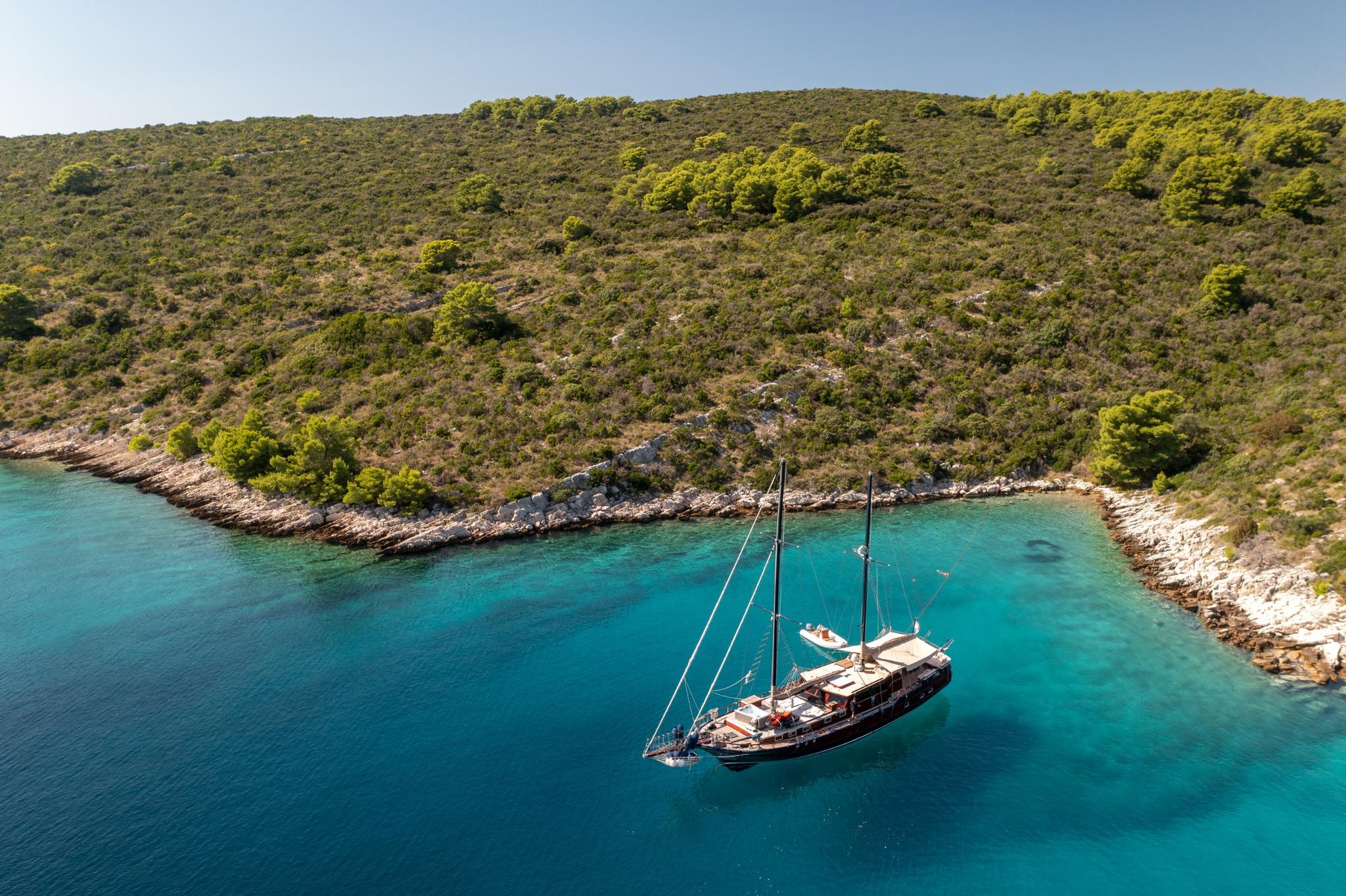 aerial view of traditional wooden gulet anchored in pristine turquoise bay surrounded by forested coastline