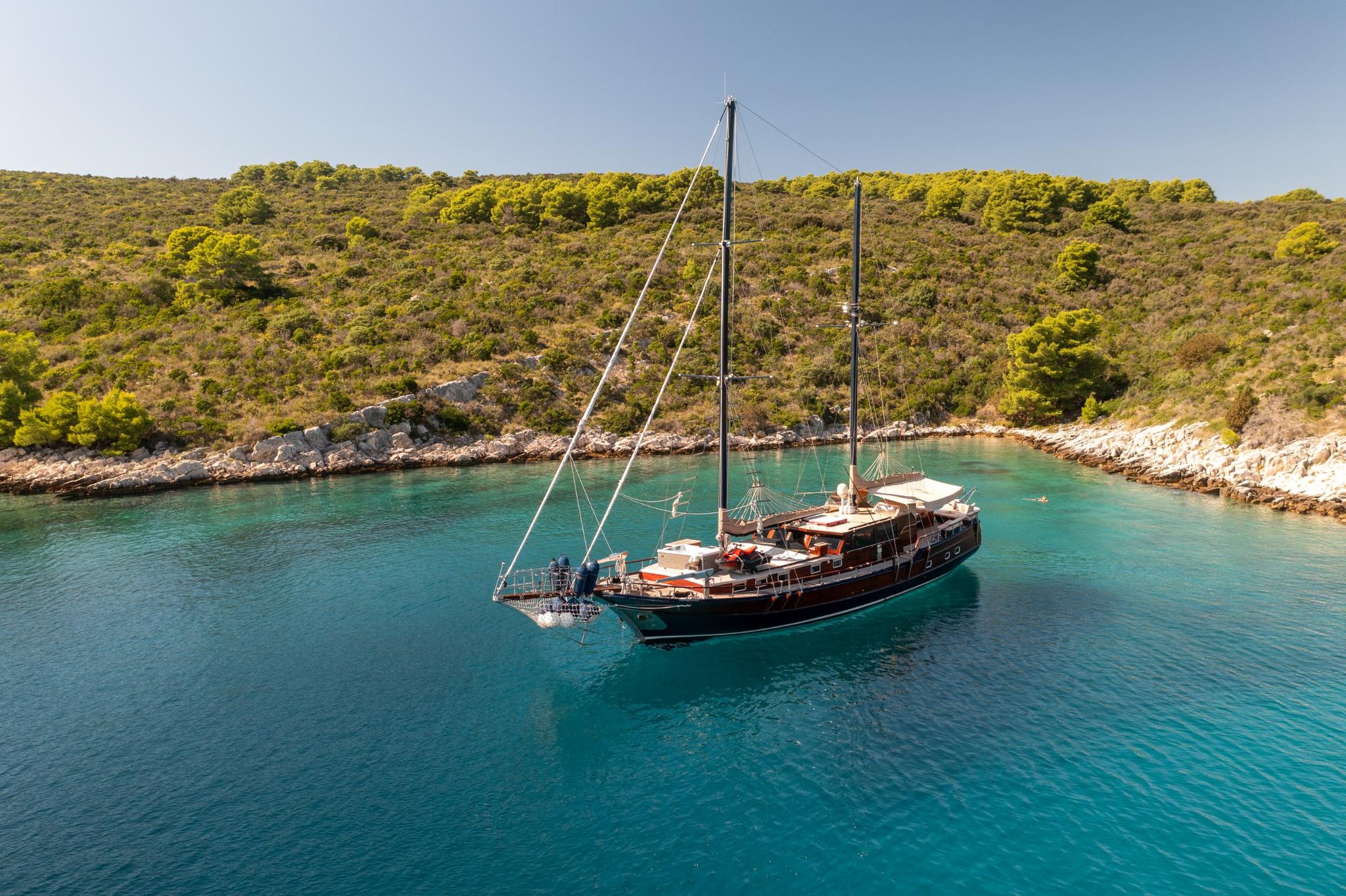 aerial view of traditional wooden gulet yacht anchored in secluded turquoise bay with forested coastline