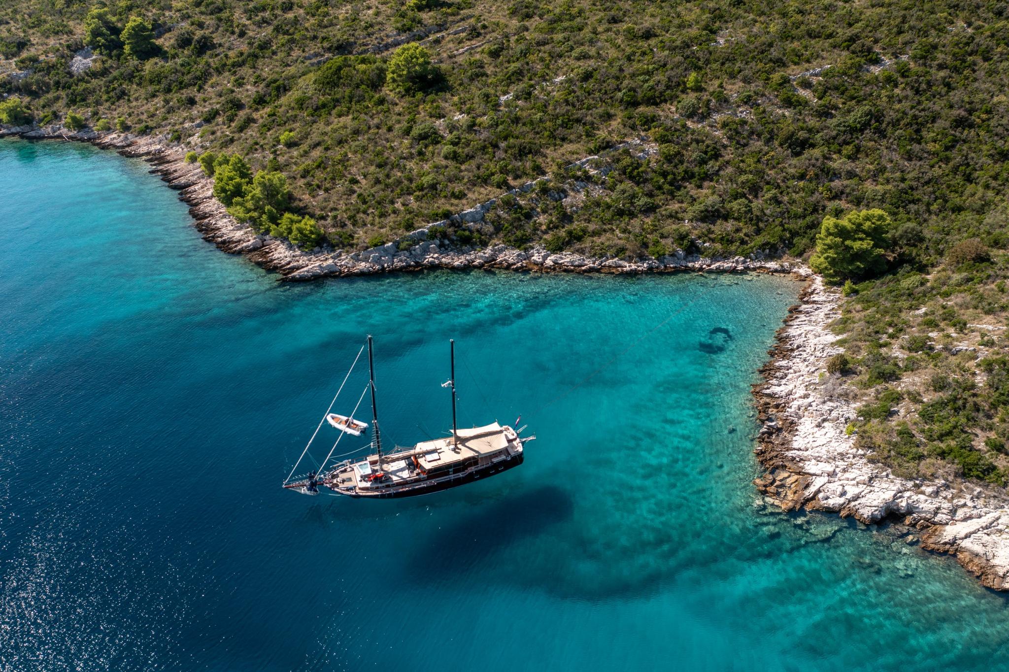 aerial view of traditional gulet yacht anchored in crystal clear turquoise bay surrounded by rocky coastline