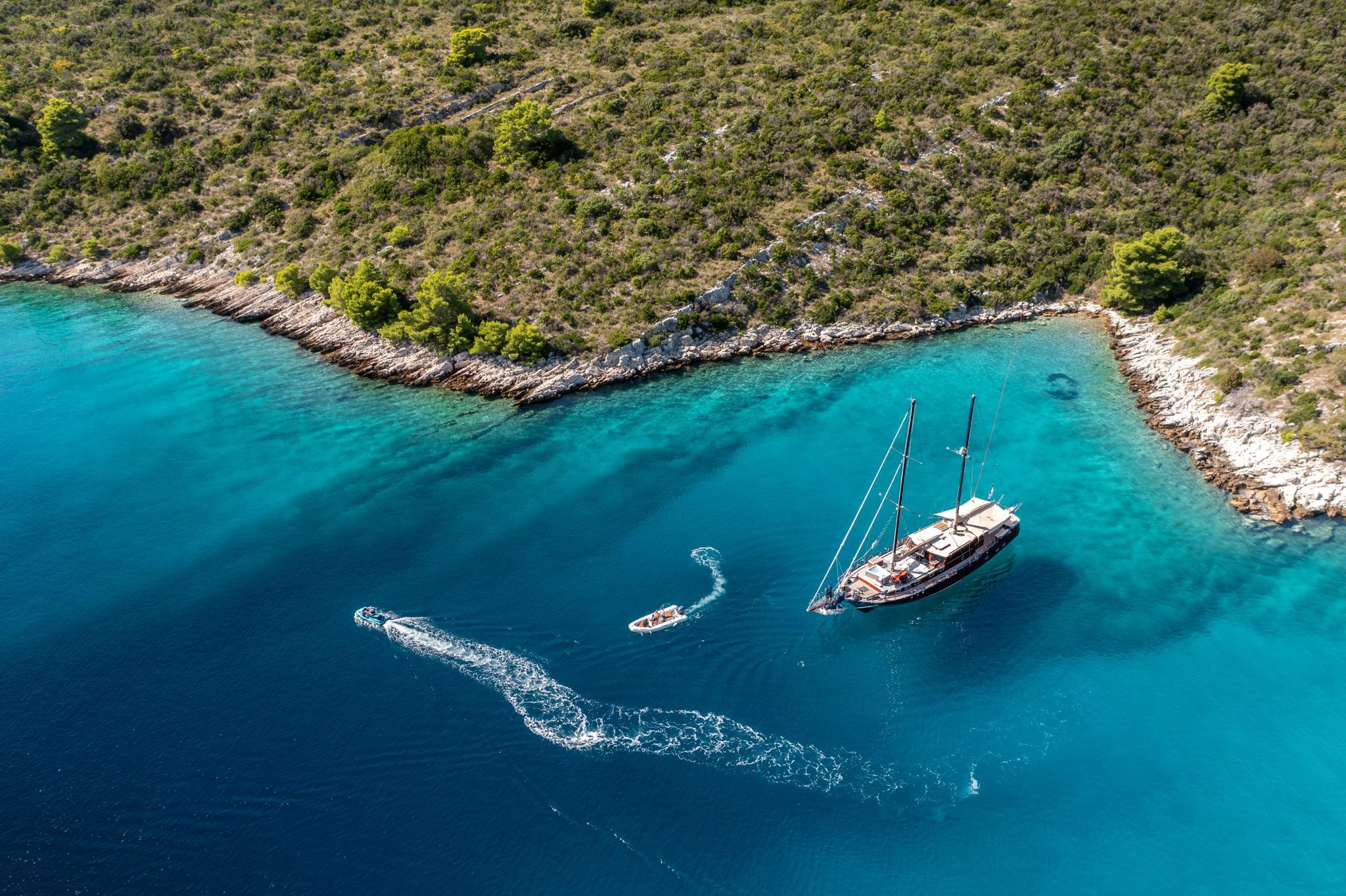 aerial view of traditional gulet yacht anchored in crystal clear turquoise bay with tender boat