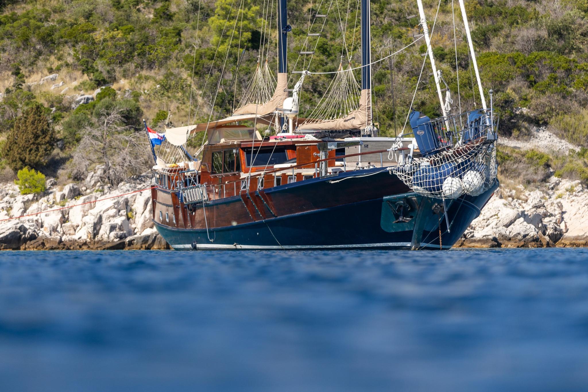 Traditional wooden gulet yacht anchored in blue waters near Mediterranean rocky coastline