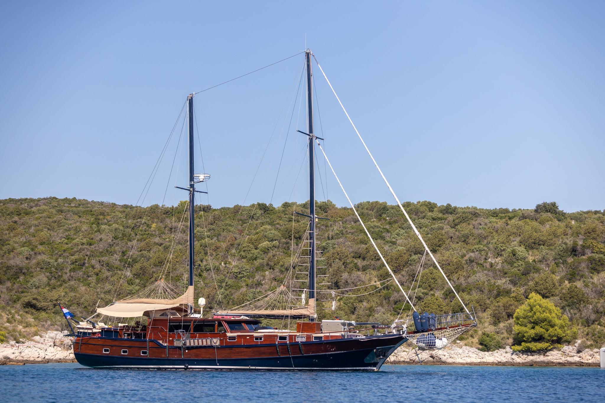 wooden gulet yacht with two masts anchored in Mediterranean bay with forested coastline