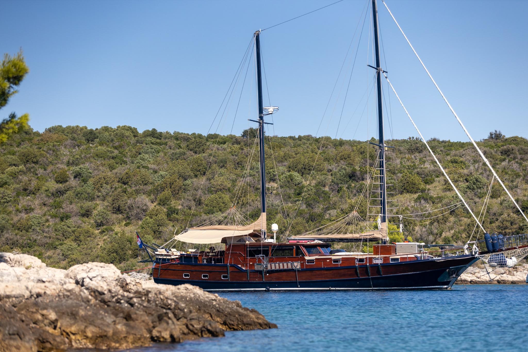 Traditional wooden gulet with two masts anchored in clear blue Mediterranean waters near rocky coastline
