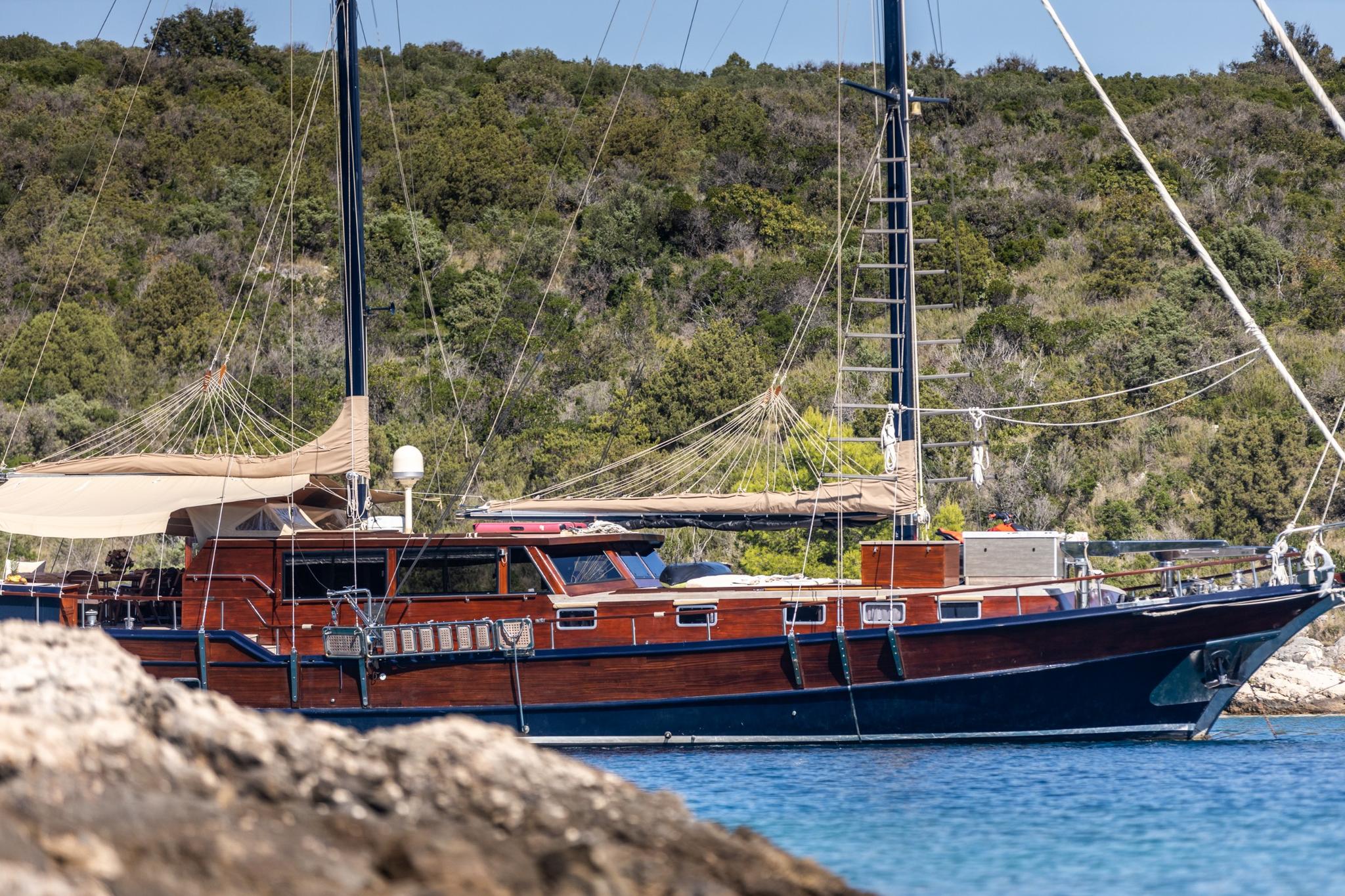 wooden gulet yacht with blue hull moored in calm bay with forested coastline