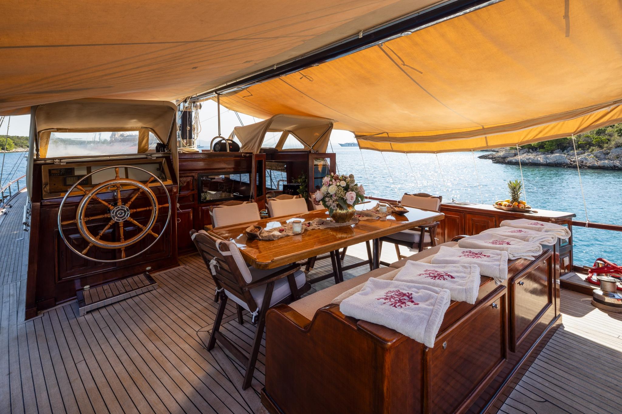gulet aft deck dining table with ship's wheel, teak decking and canvas awning