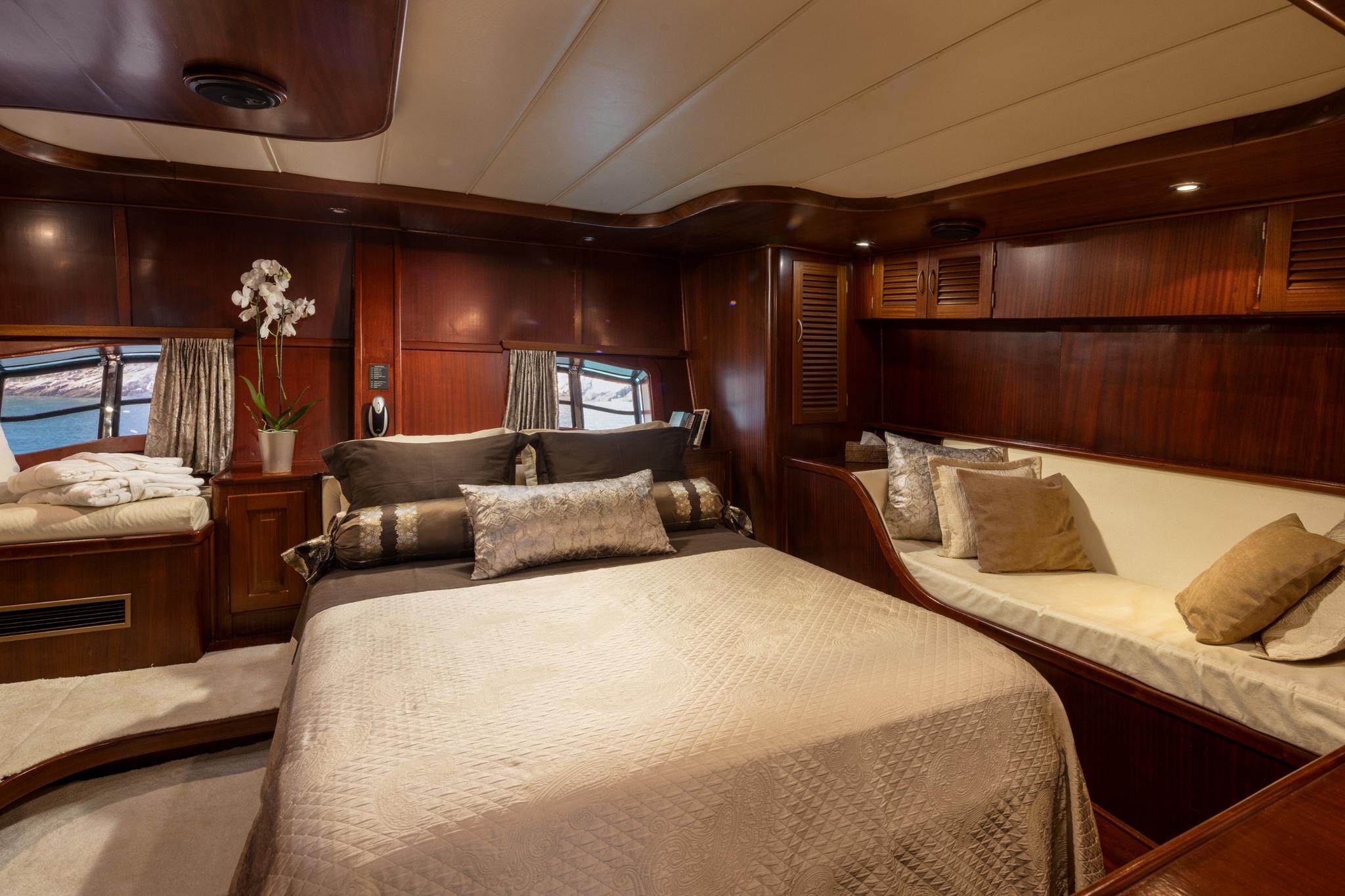 yacht cabin interior with double bed, built-in seating, rich wood paneling and portholes