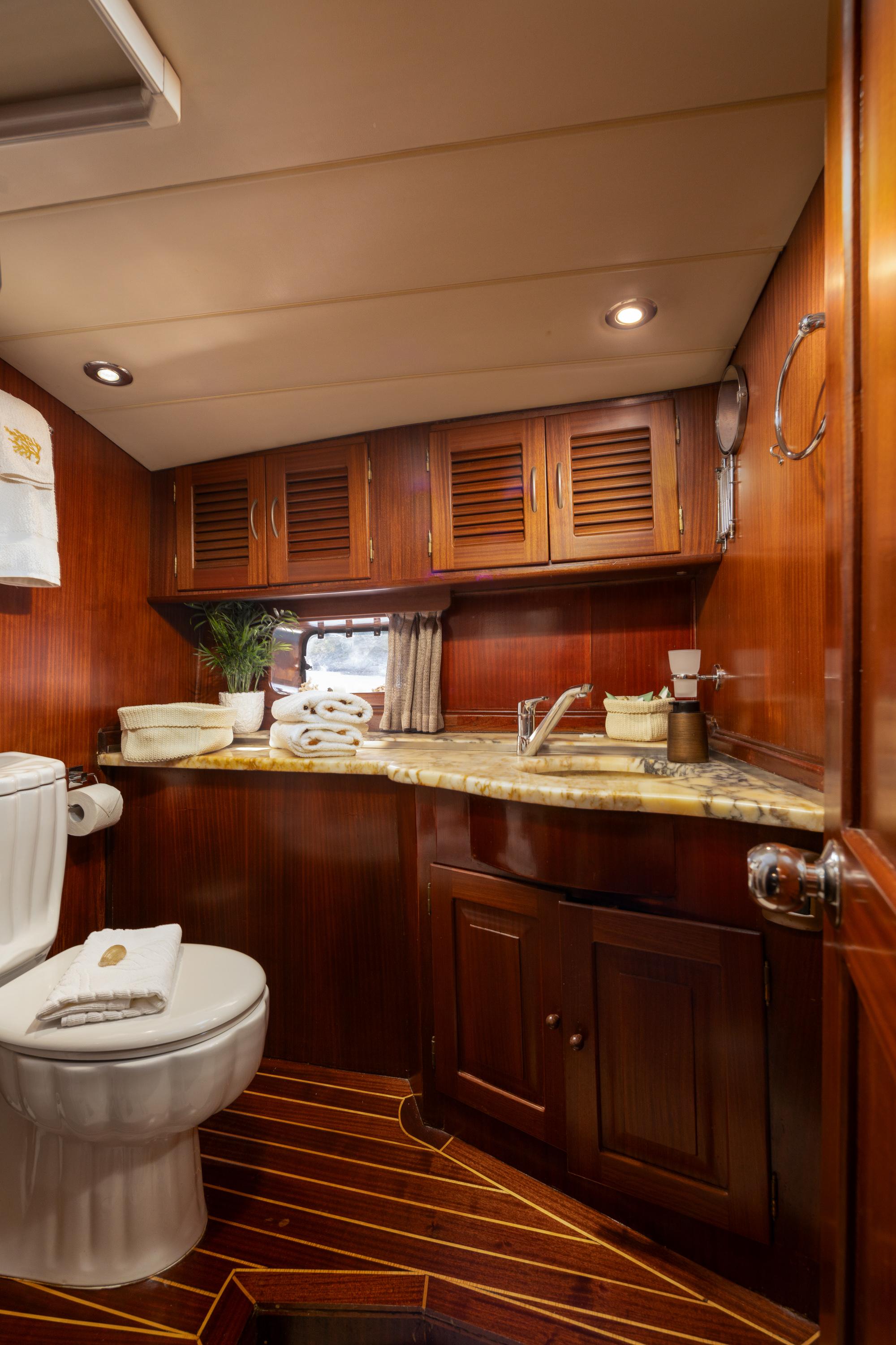 compact yacht bathroom featuring white toilet, marble vanity countertop, and rich mahogany cabinetry