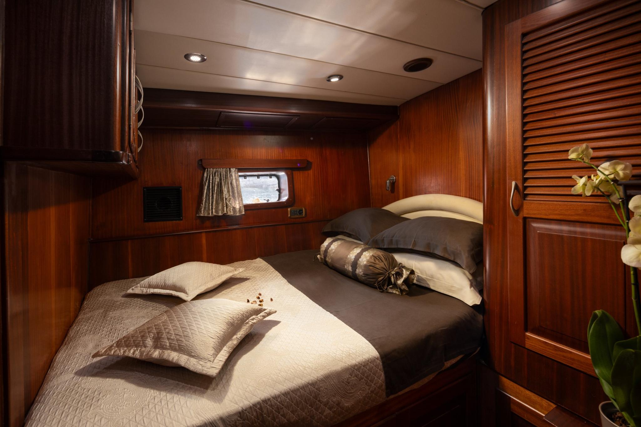 yacht cabin with double bed, cream bedding, wooden walls and nautical porthole window