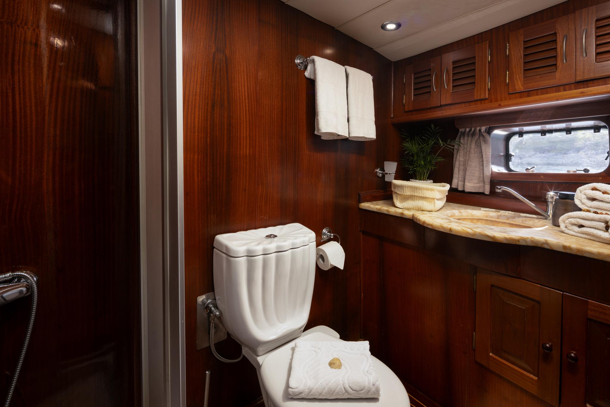 yacht bathroom with white toilet, marble countertop vanity, and rich wood paneling