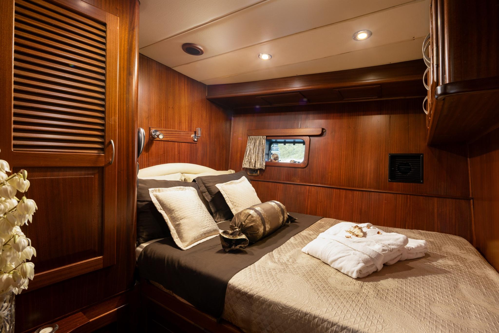 yacht guest cabin with double bed, warm wood paneling and circular porthole window