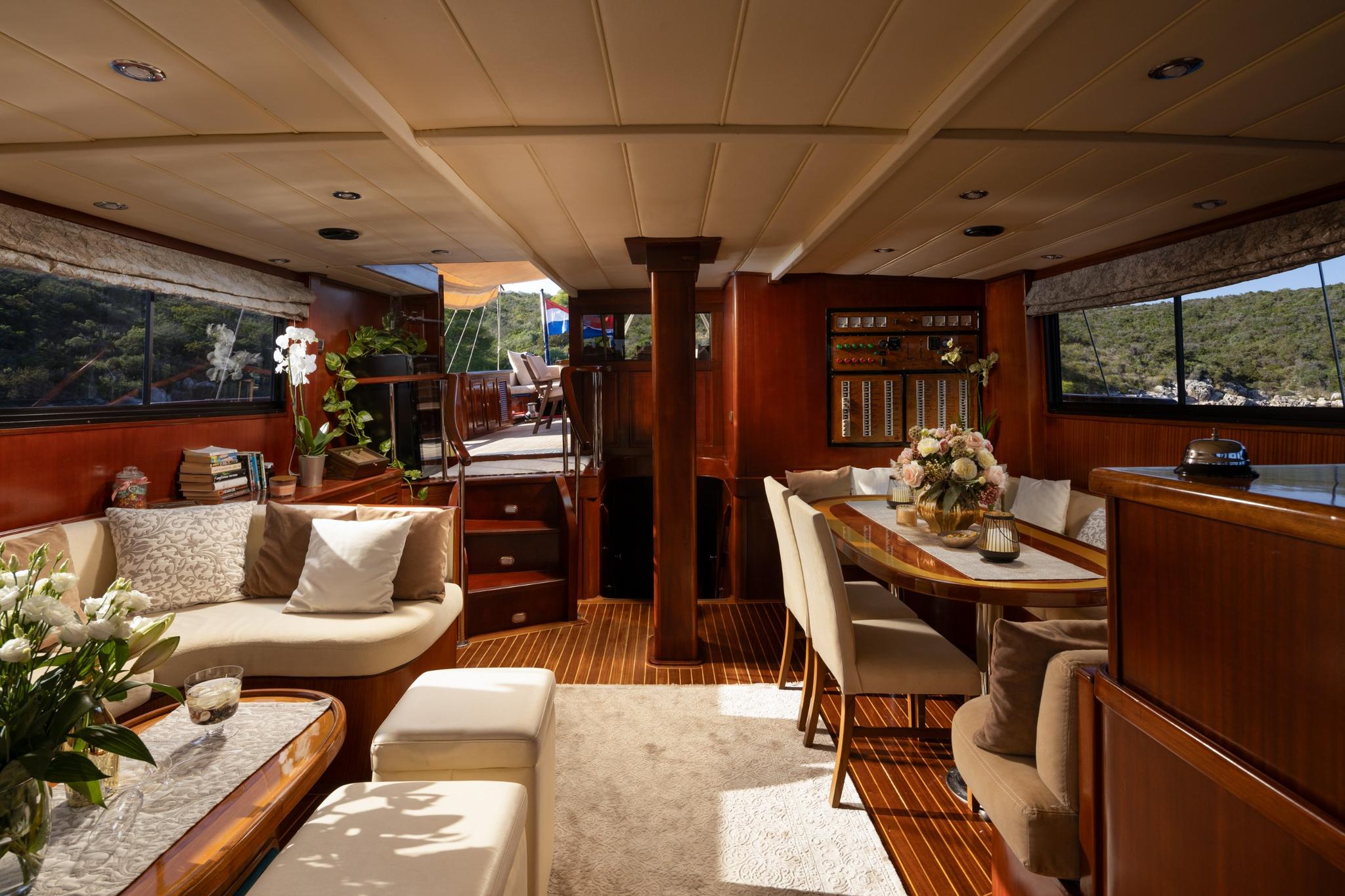 yacht main salon interior featuring dining table, cream sofas, and teak flooring with panoramic windows