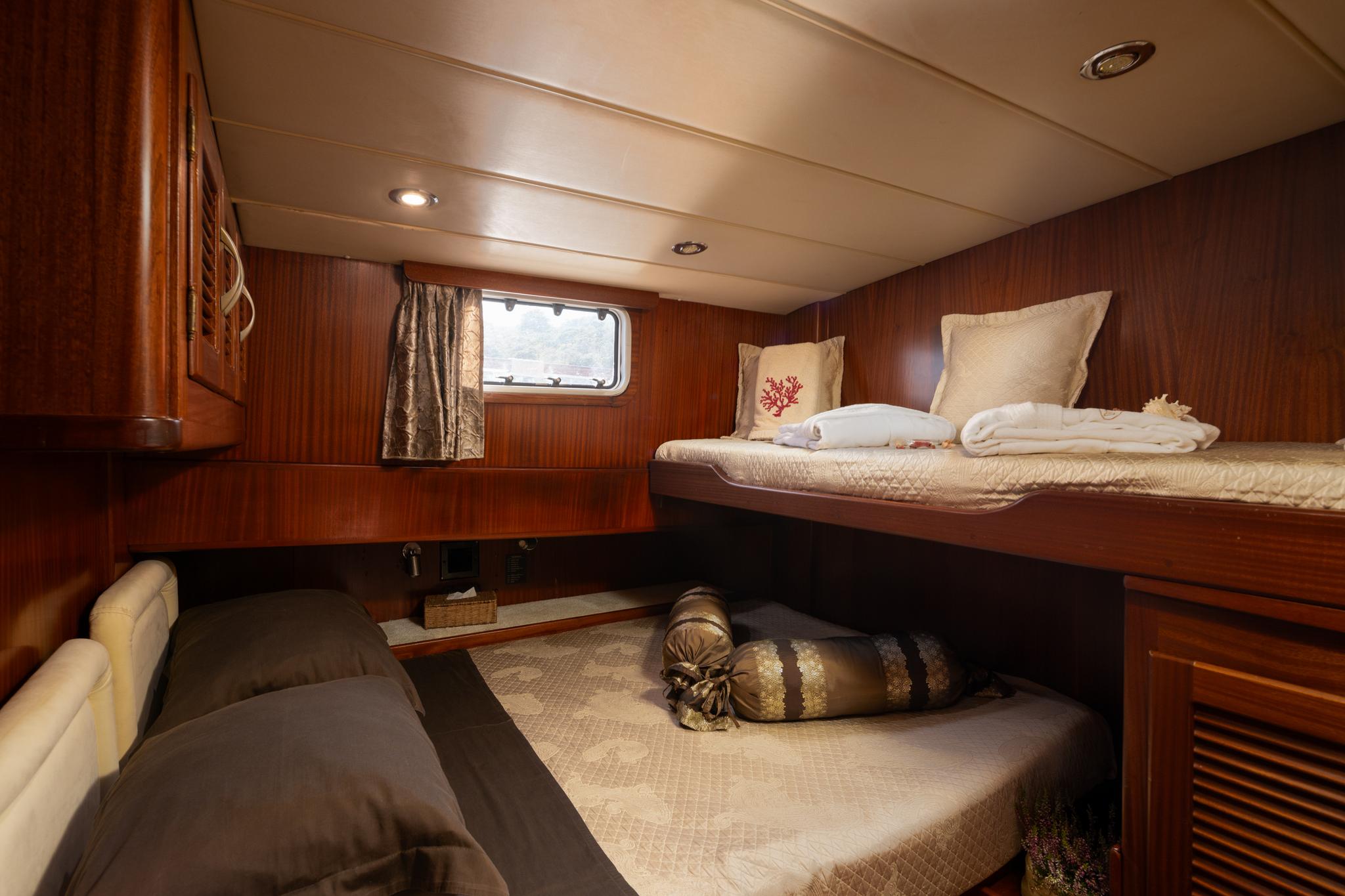 yacht guest cabin featuring upper and lower bunk beds with cream bedding and porthole window