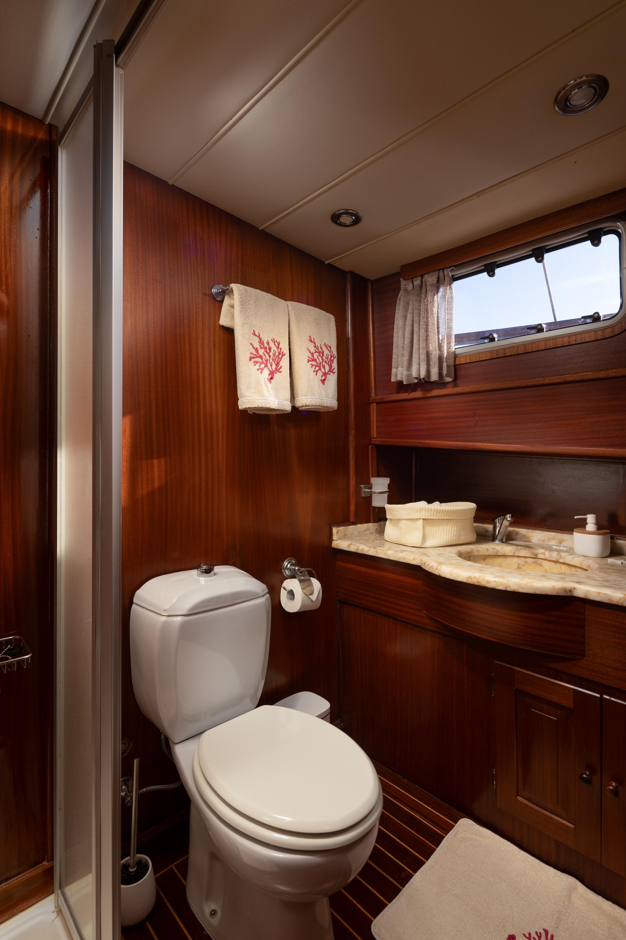 yacht bathroom interior with white toilet, marble countertop vanity, and coral-embroidered towels