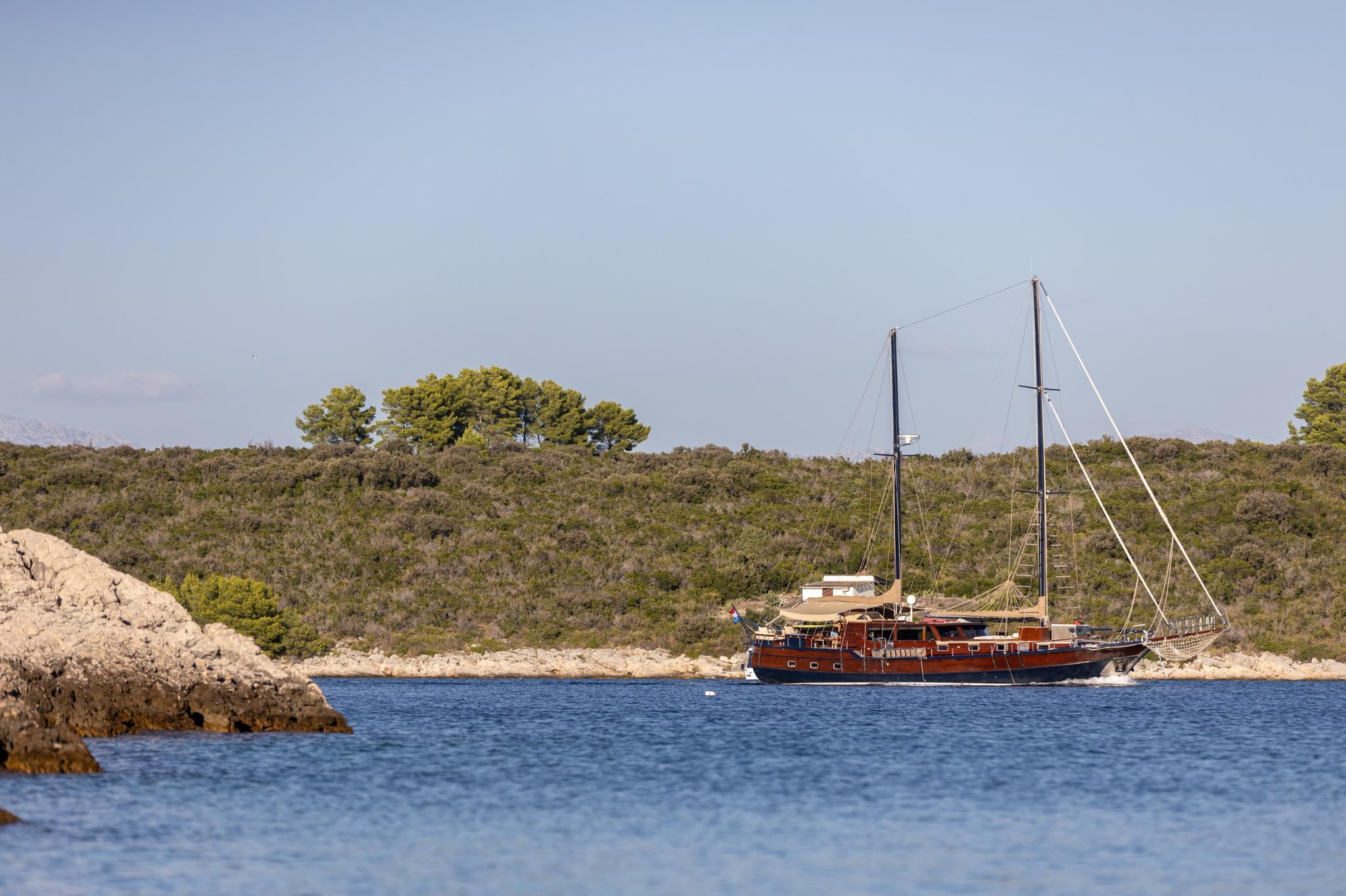 Traditional wooden gulet with two masts anchored in secluded Mediterranean bay with rocky coastline