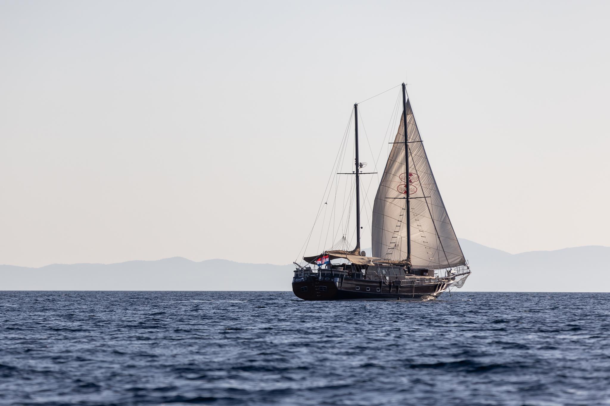 Traditional wooden gulet with two masts and beige sails sailing on blue Mediterranean waters