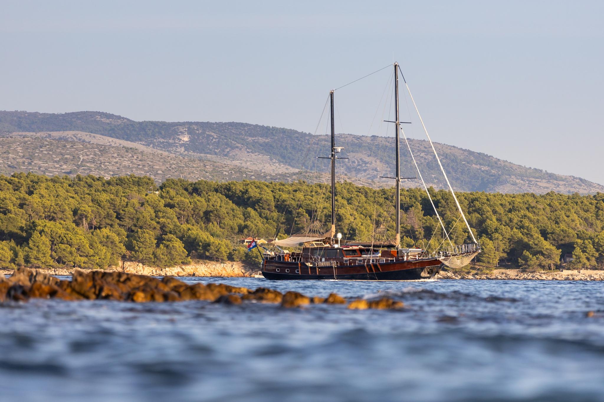 wooden gulet yacht anchored in calm Mediterranean waters with forested coastline and mountains