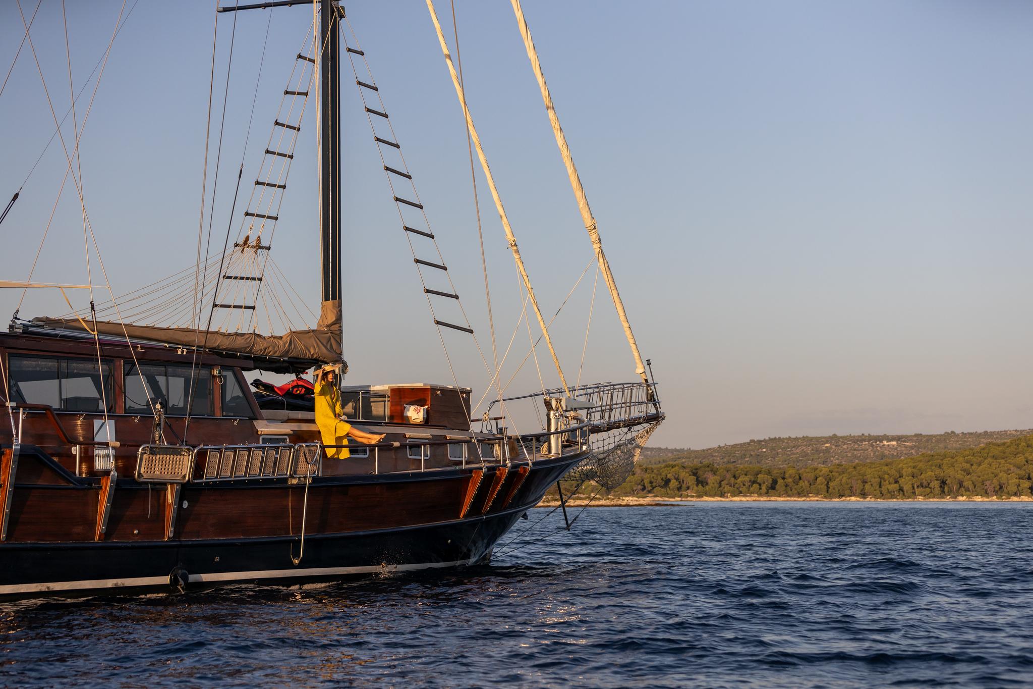 wooden gulet yacht with traditional rigging anchored in Mediterranean bay at golden hour