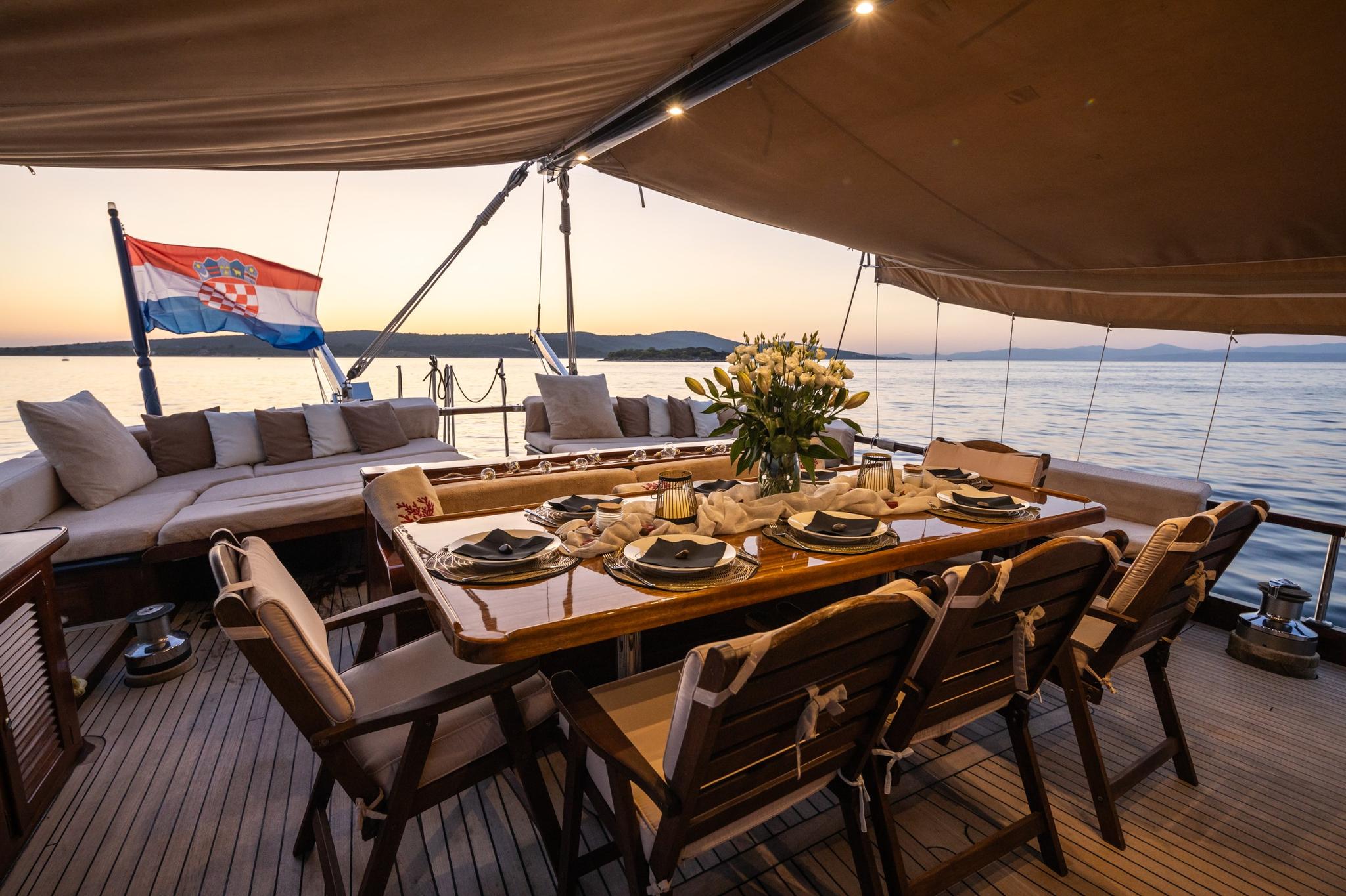 gulet aft deck with formal dining table, seating area, and Croatian flag at sunset