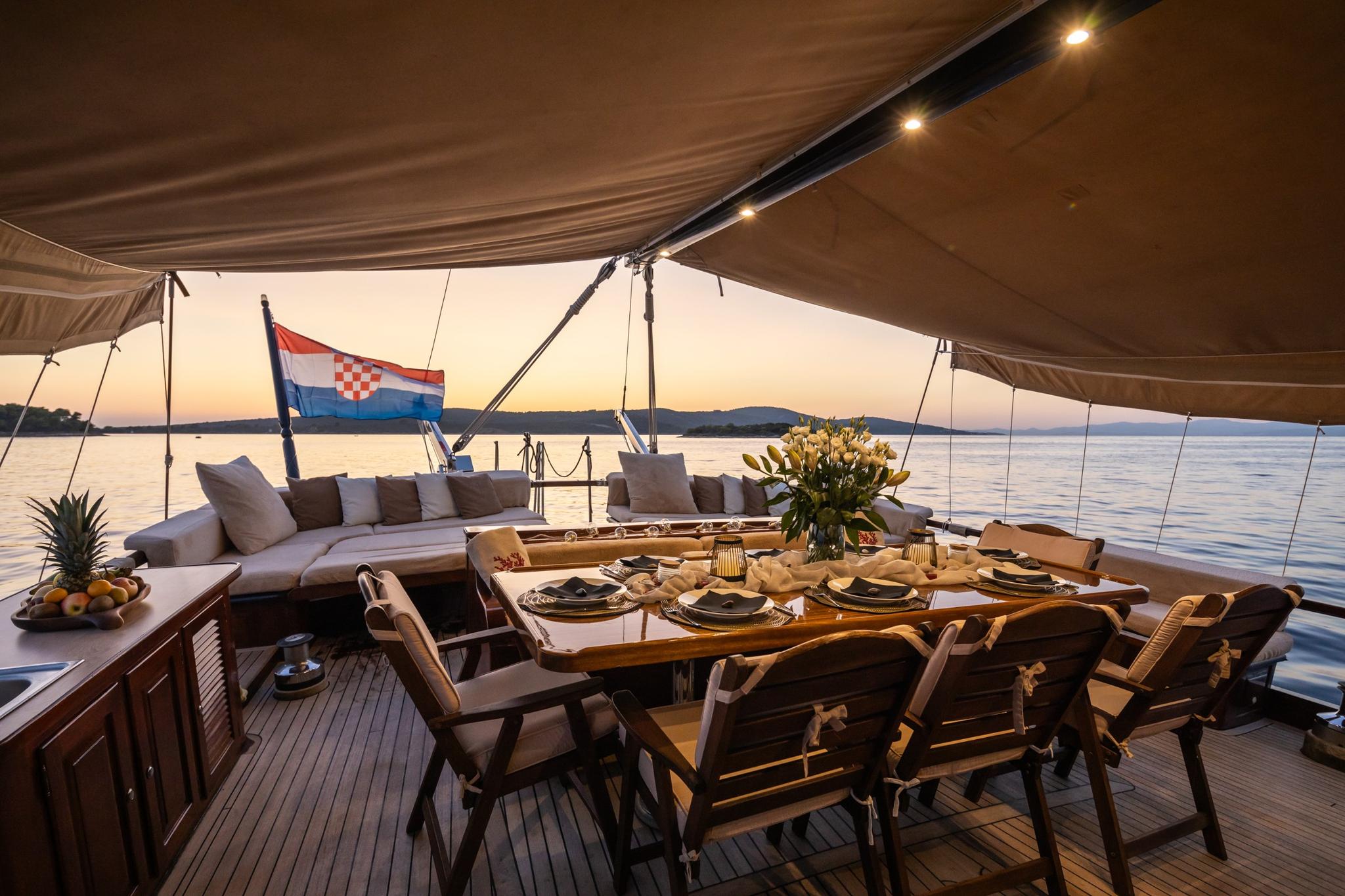 yacht aft deck with outdoor dining table and cushioned seating area at sunset