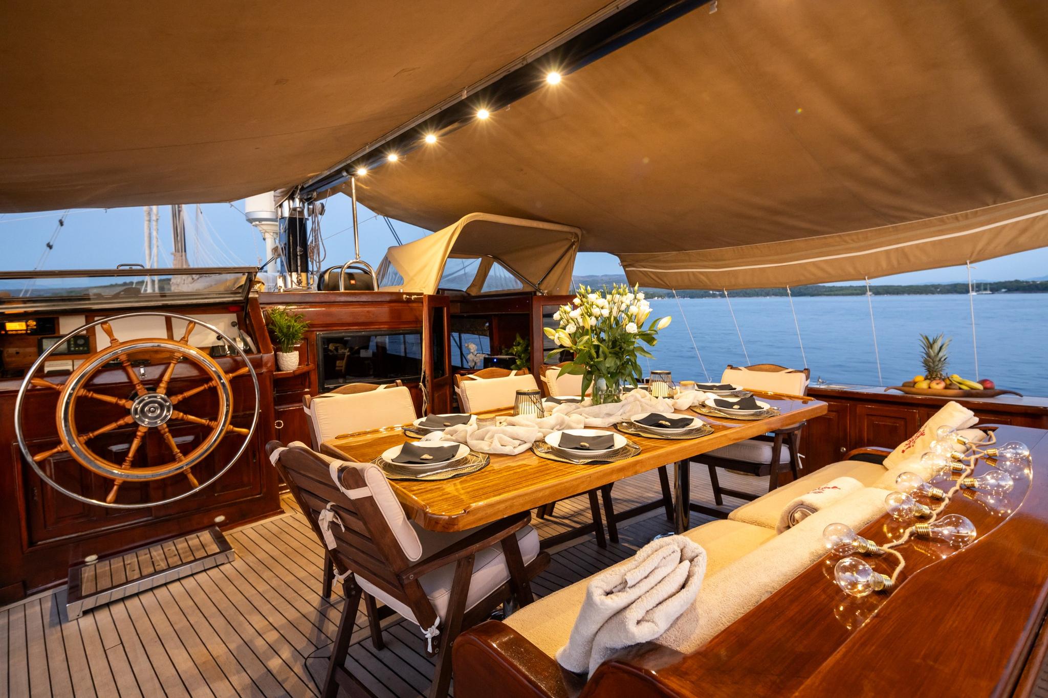 aft deck dining table with place settings, wooden helm wheel, and cream awning overhead