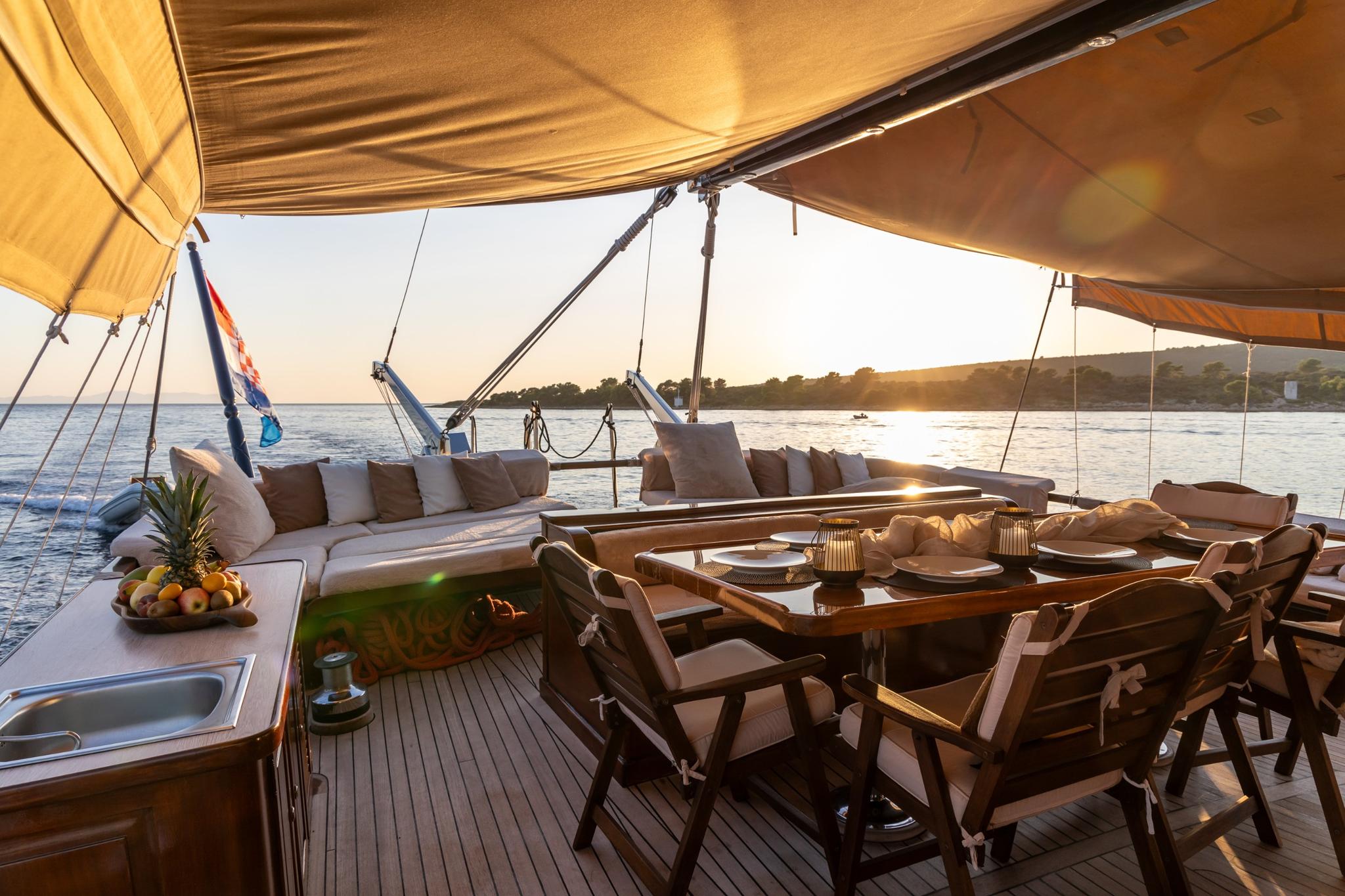 yacht aft deck with outdoor dining table, cushioned seating area under canvas awning at sunset