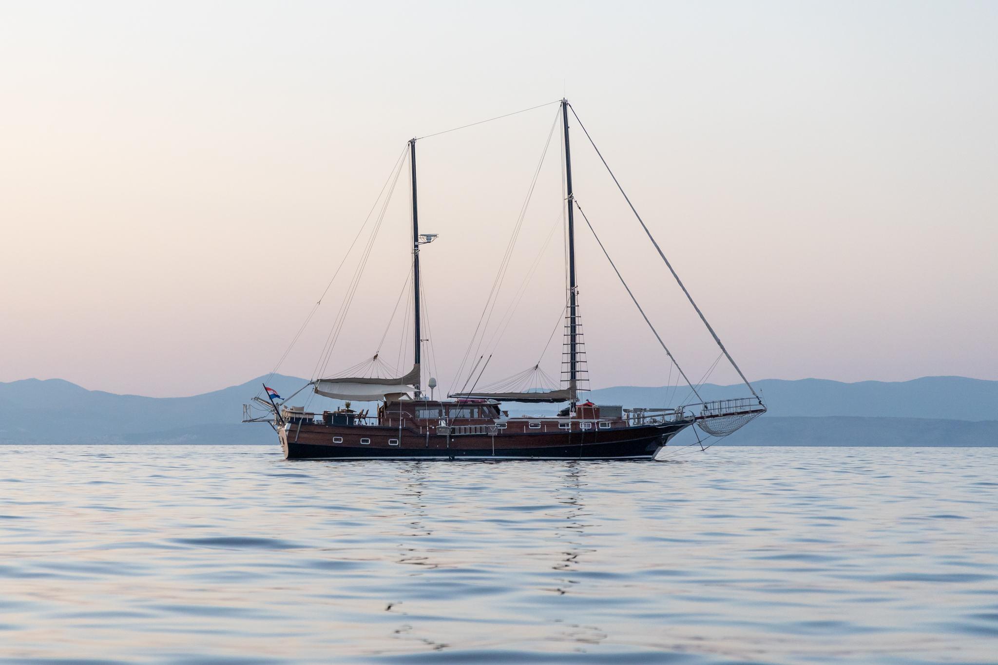 wooden gulet yacht anchored in calm waters with mountains in background at sunset