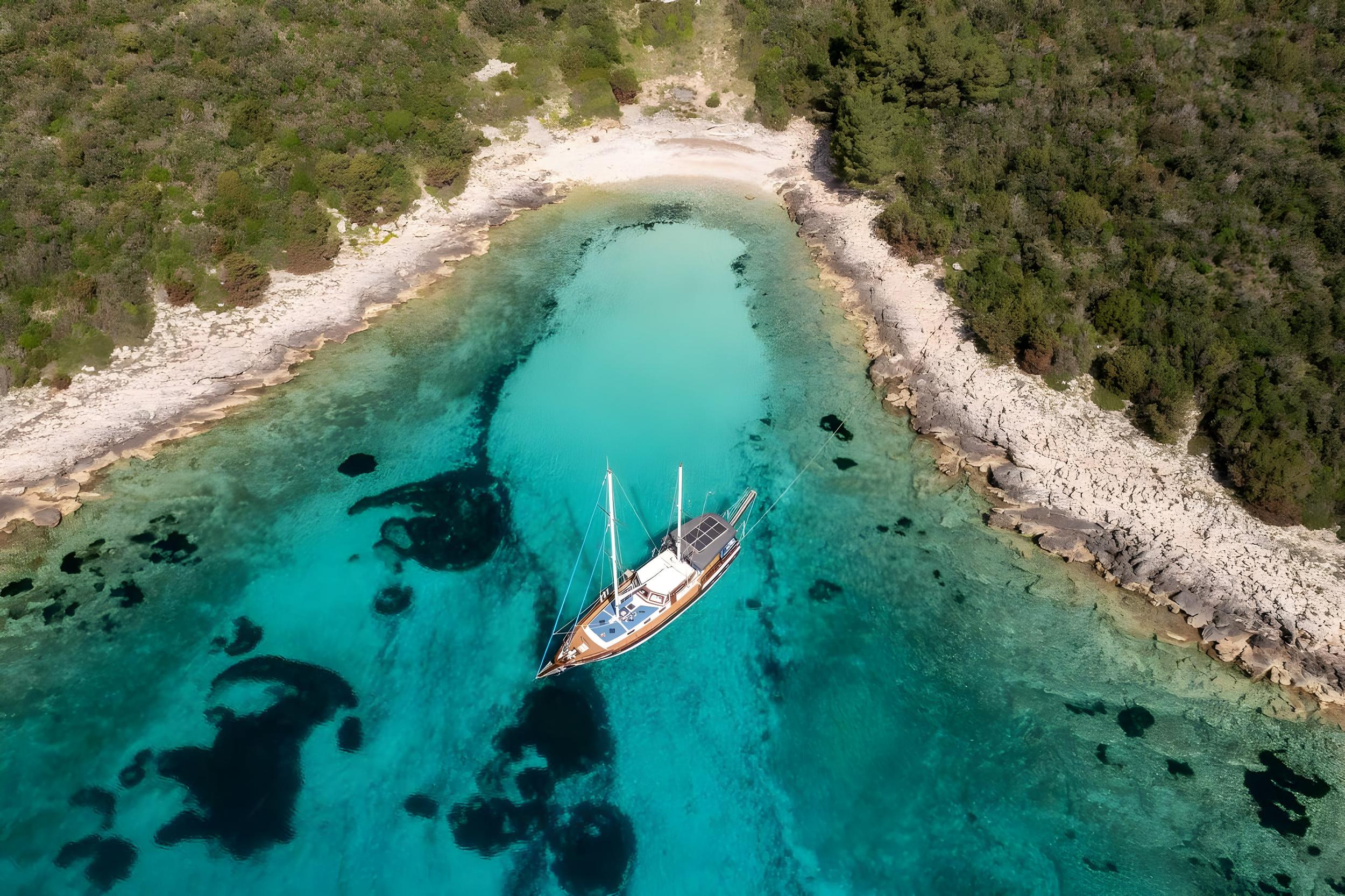 aerial view of traditional gulet yacht anchored in protected turquoise bay surrounded by rocky coastline