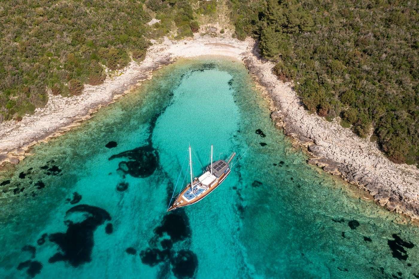 aerial view of traditional gulet yacht anchored in protected turquoise bay surrounded by rocky coastline