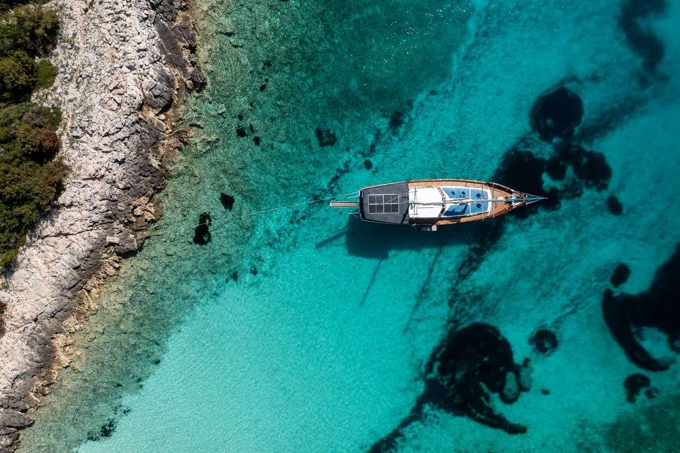 aerial view of traditional gulet yacht anchored in crystal clear turquoise bay near rocky coastline