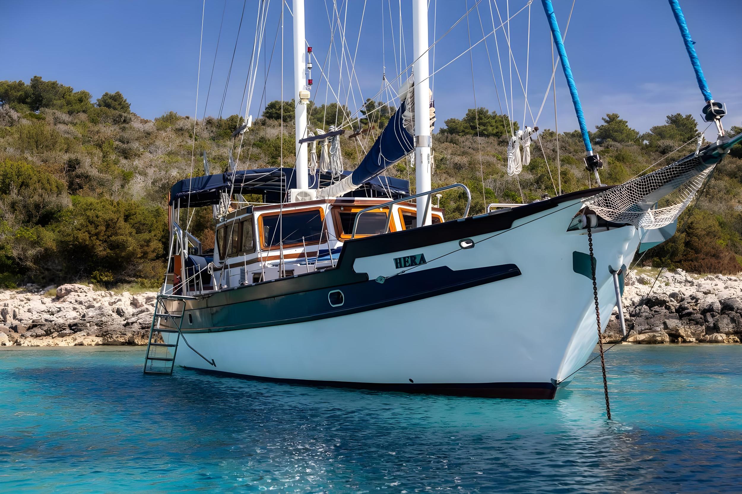White and green traditional gulet yacht anchored in crystal clear turquoise waters near rocky coastline