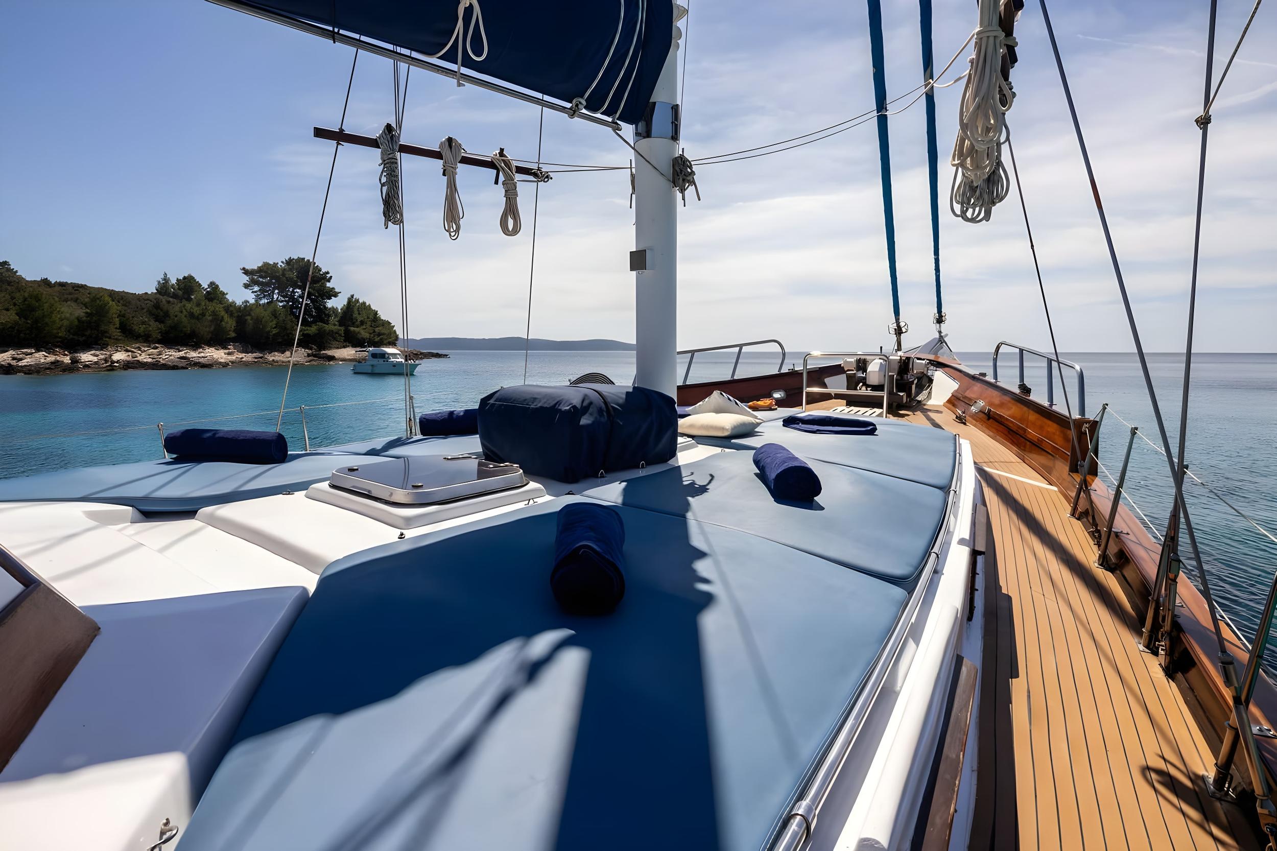 Forward sun deck with white cushioned loungers and navy pillows on sailing yacht