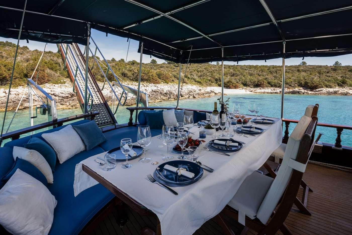 formal dining table with white tablecloth, wine glasses, dark plates and wine bottles on gulet deck