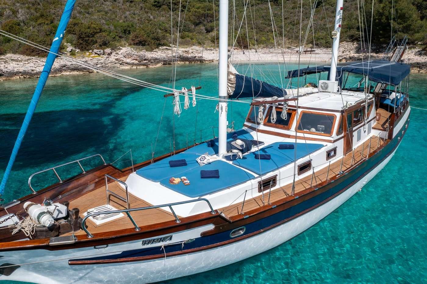 Traditional wooden gulet with blue cushioned deck areas anchored in crystal clear turquoise bay