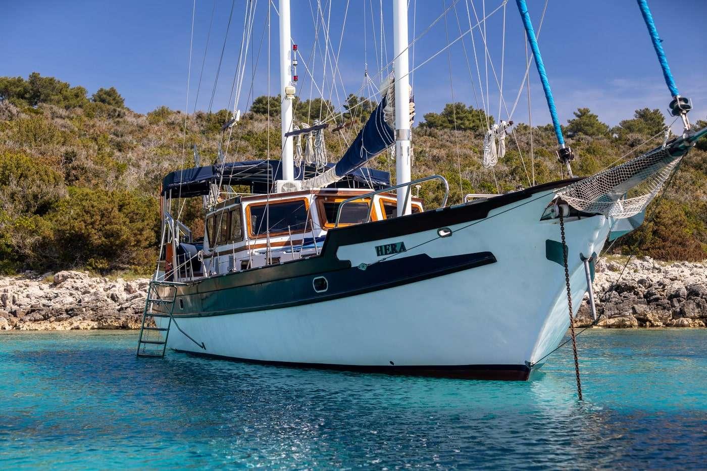 White gulet yacht with green trim anchored in crystal clear turquoise waters near rocky coastline