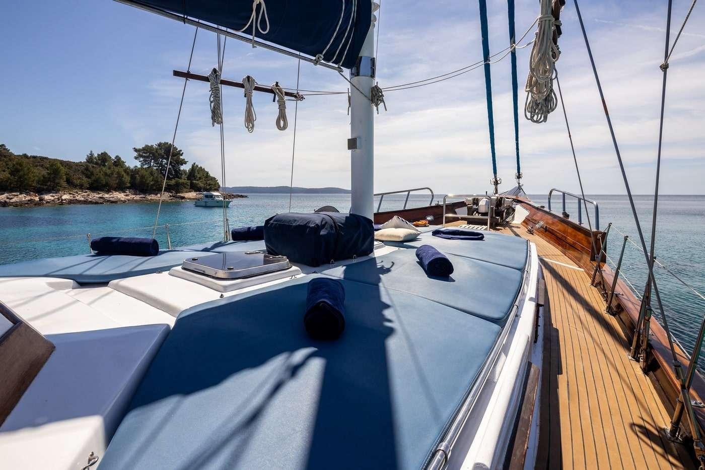Gulet bow deck with white cushioned loungers, sailing mast, and crystal clear turquoise waters