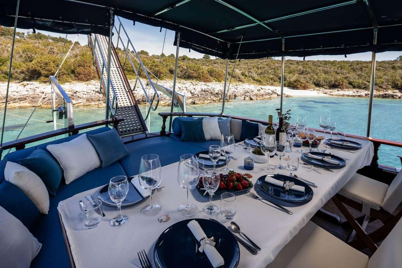 yacht dining table set with wine glasses, plates, and strawberries overlooking turquoise bay
