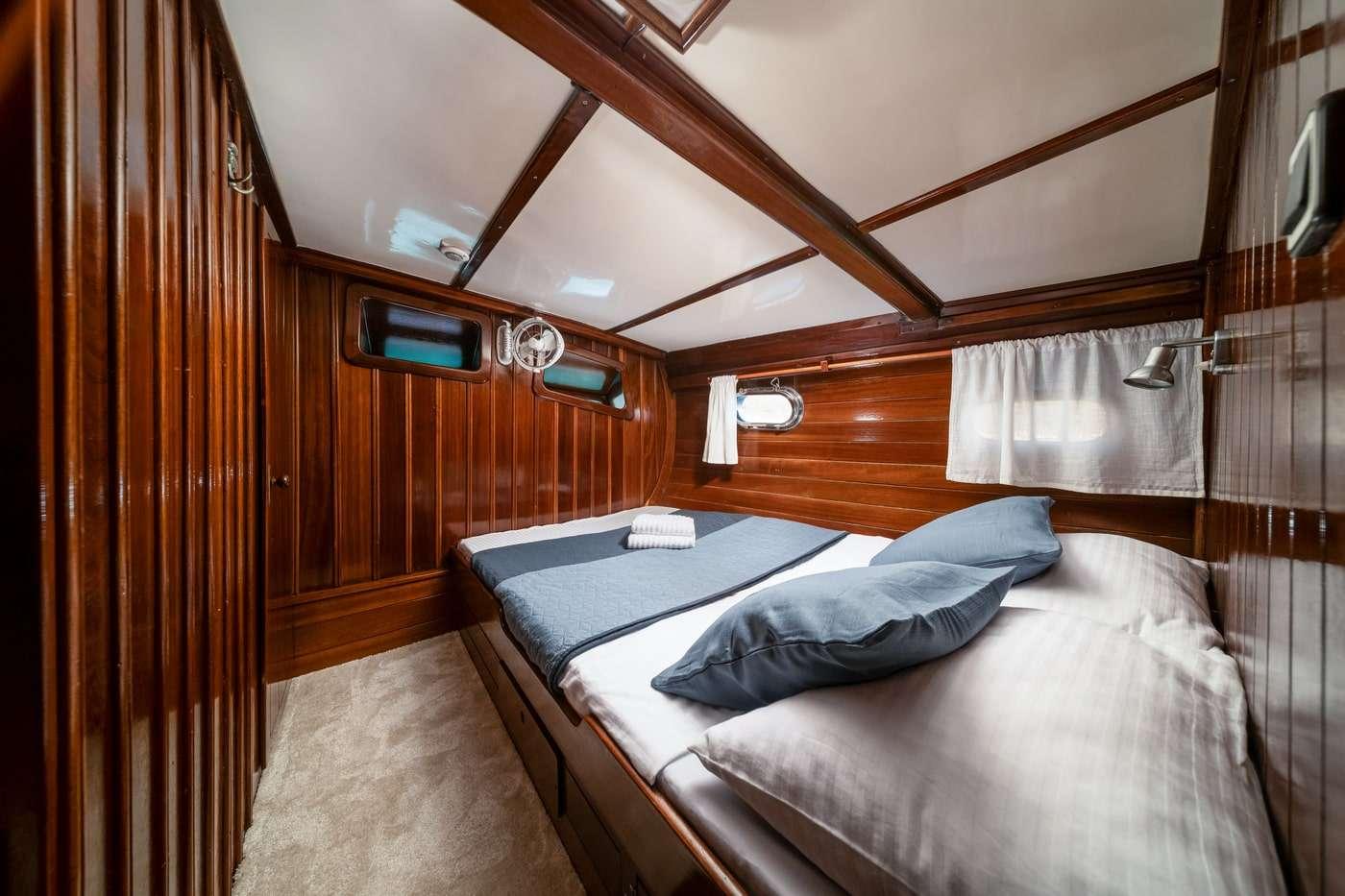 yacht guest cabin with double bed, rich wood paneling and porthole windows